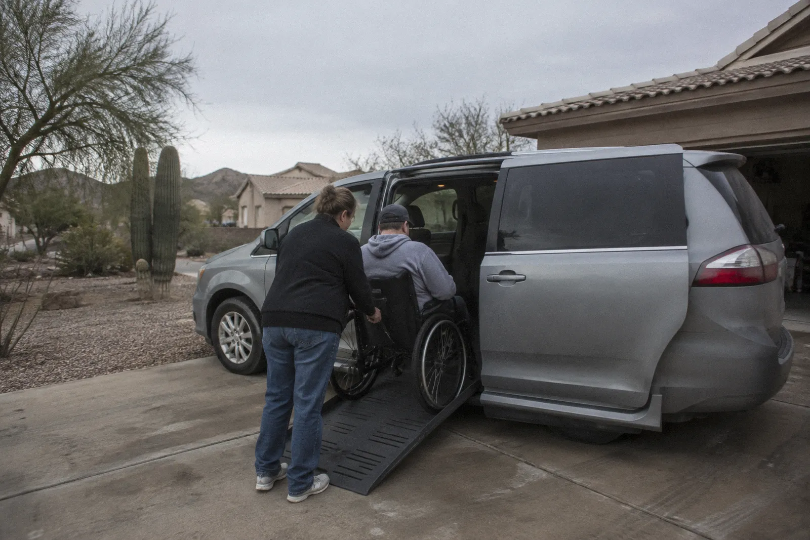 A wheelchair accessible van with its side ramp deployed in a home driveway, desert landscaping