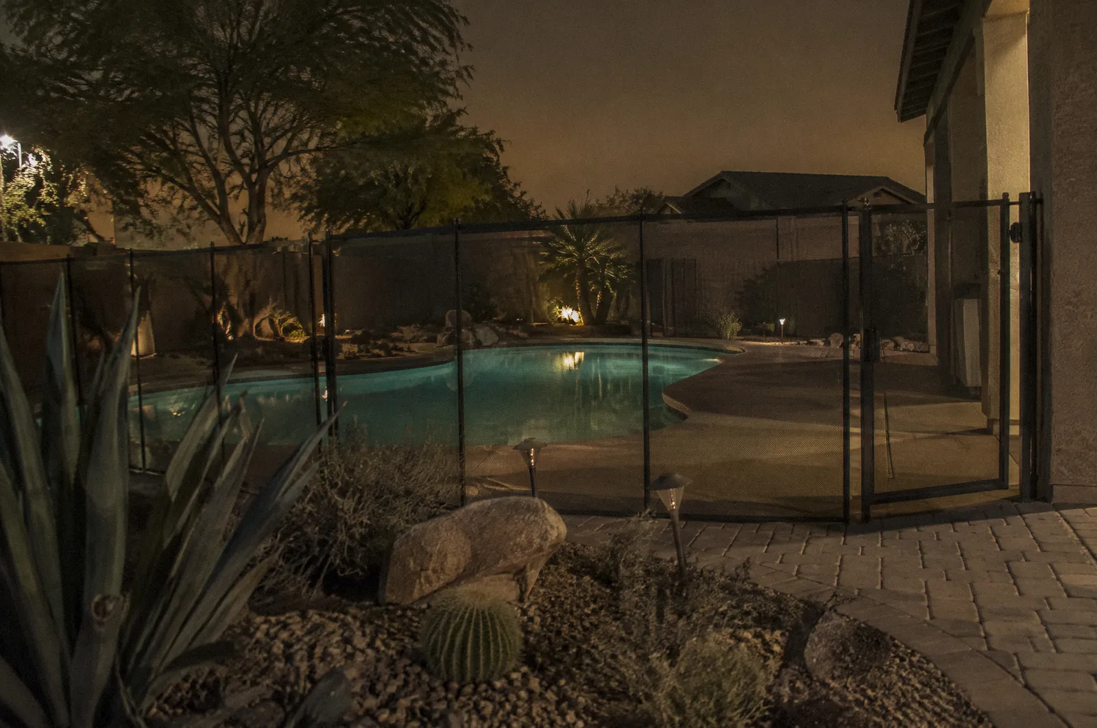 A backyard pool with a pool fence and self-closing gate, desert landscaping, calm water, no people