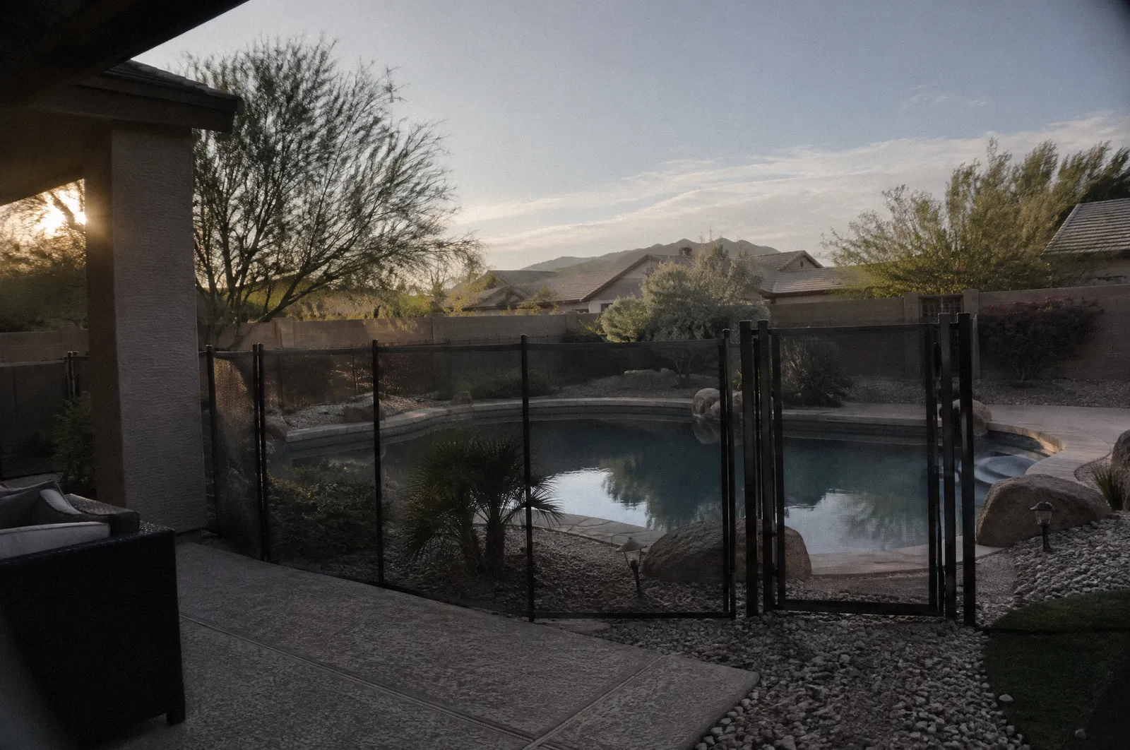 A backyard pool with a pool fence and self-closing gate, desert landscaping, calm water, no people