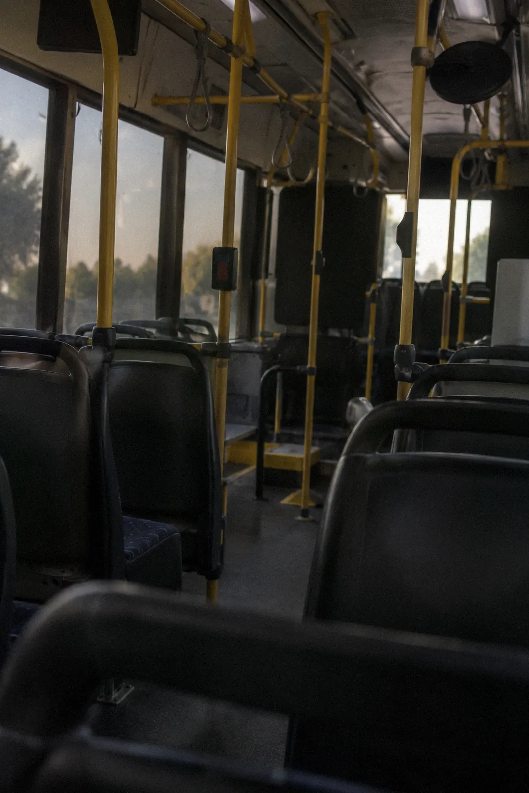 The empty interior of a city transit bus, rows of seats and yellow handrails, light through tinted windows, no readable text