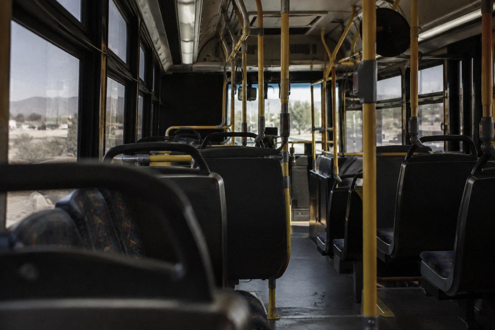 The empty interior of a city transit bus, rows of seats and yellow handrails, light through tinted windows, no readable text