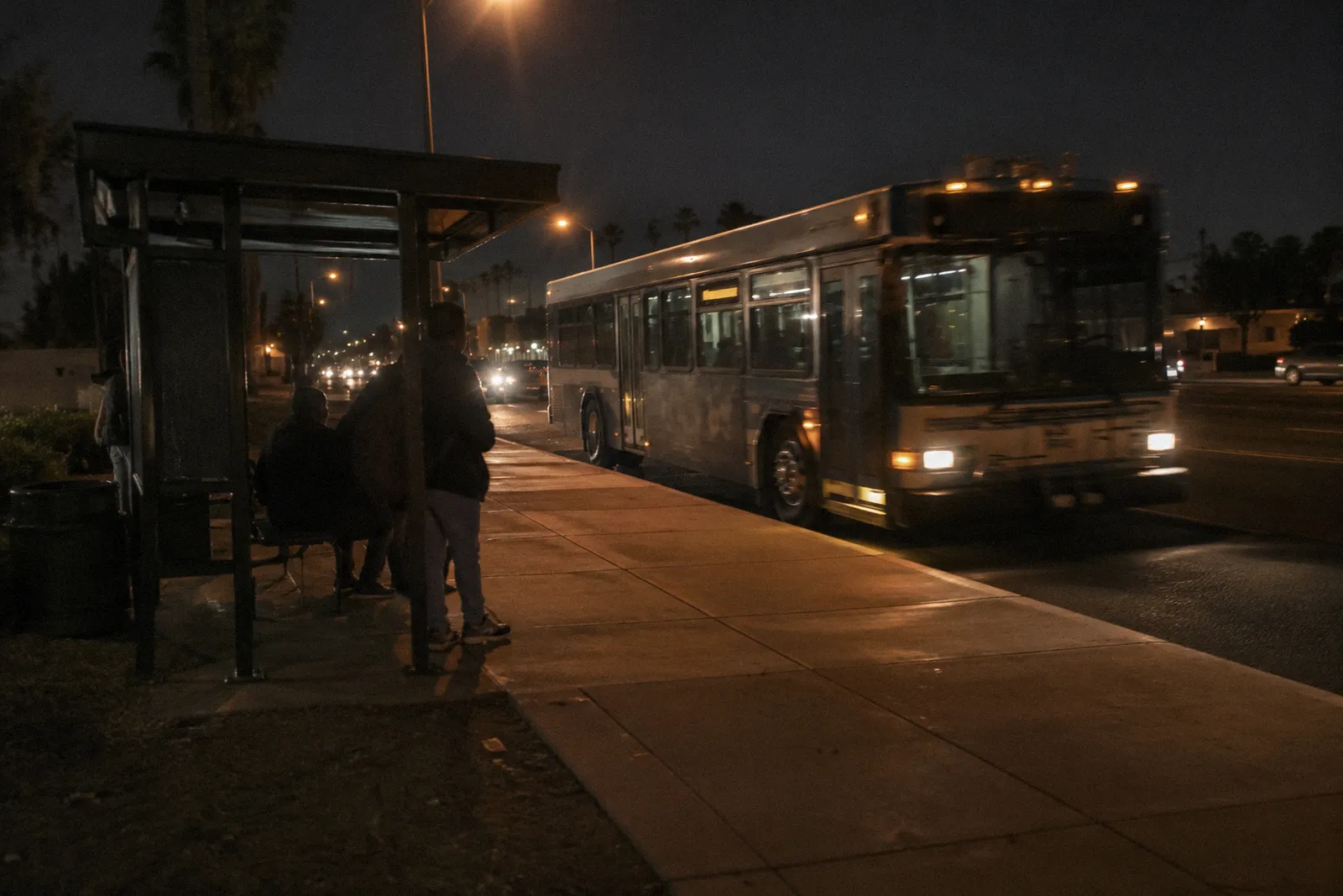 A city bus pulling into a shaded bus shelter on a wide Phoenix-area arterial road, motion blur, no readable text