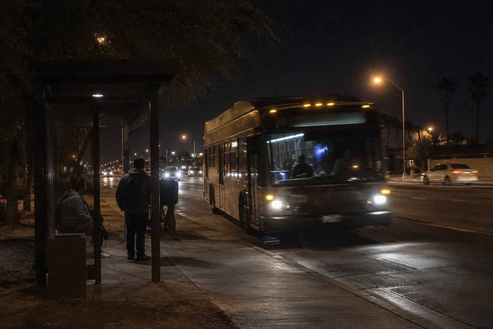 A city bus pulling into a shaded bus shelter on a wide Phoenix-area arterial road, motion blur, no readable text