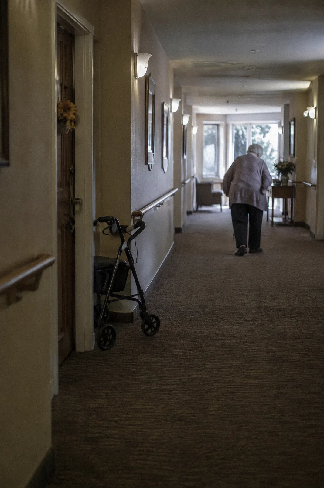 A quiet assisted living hallway with handrails and a walker by a door, soft light
