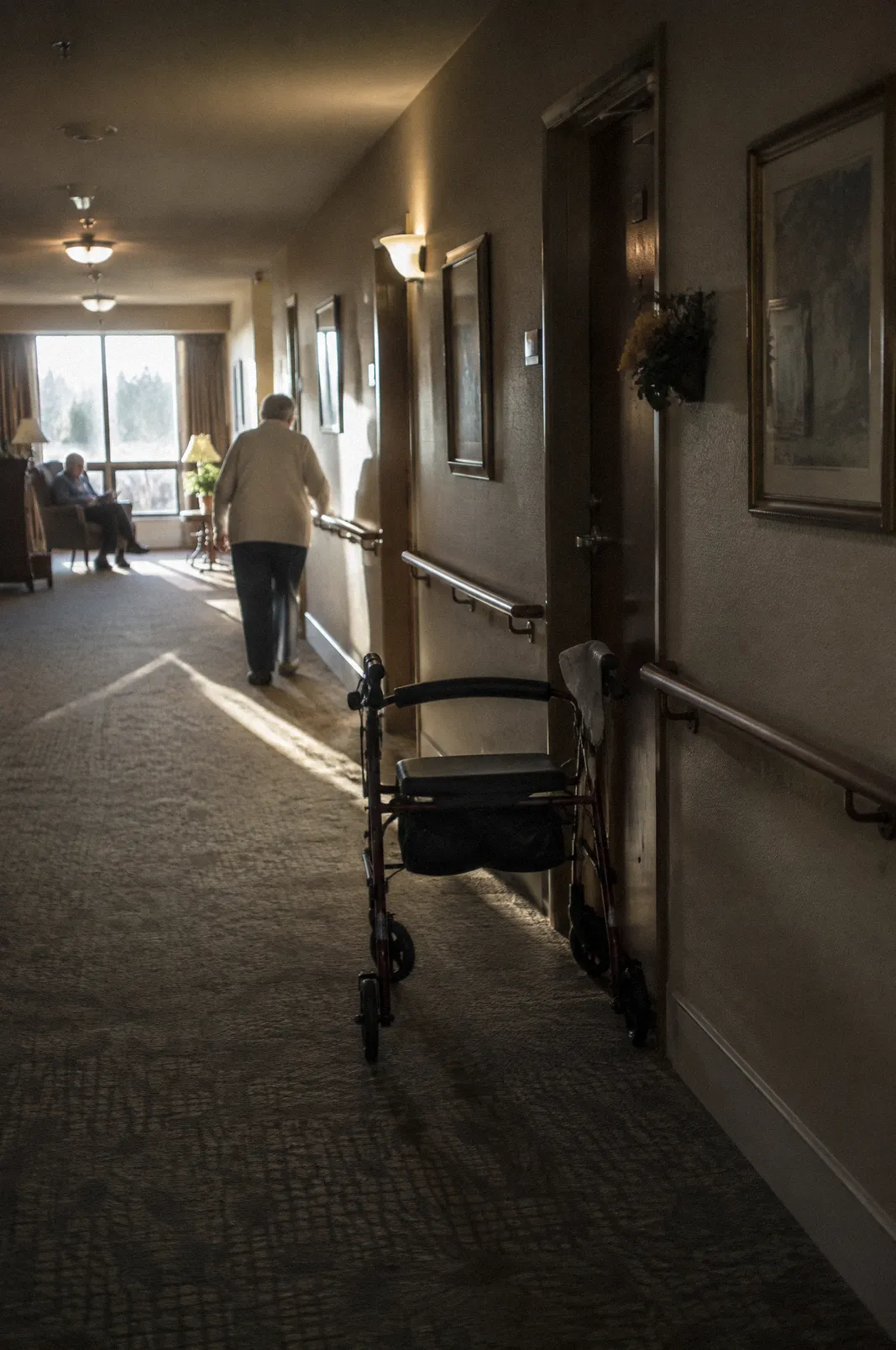 A quiet assisted living hallway with handrails and a walker by a door, soft light