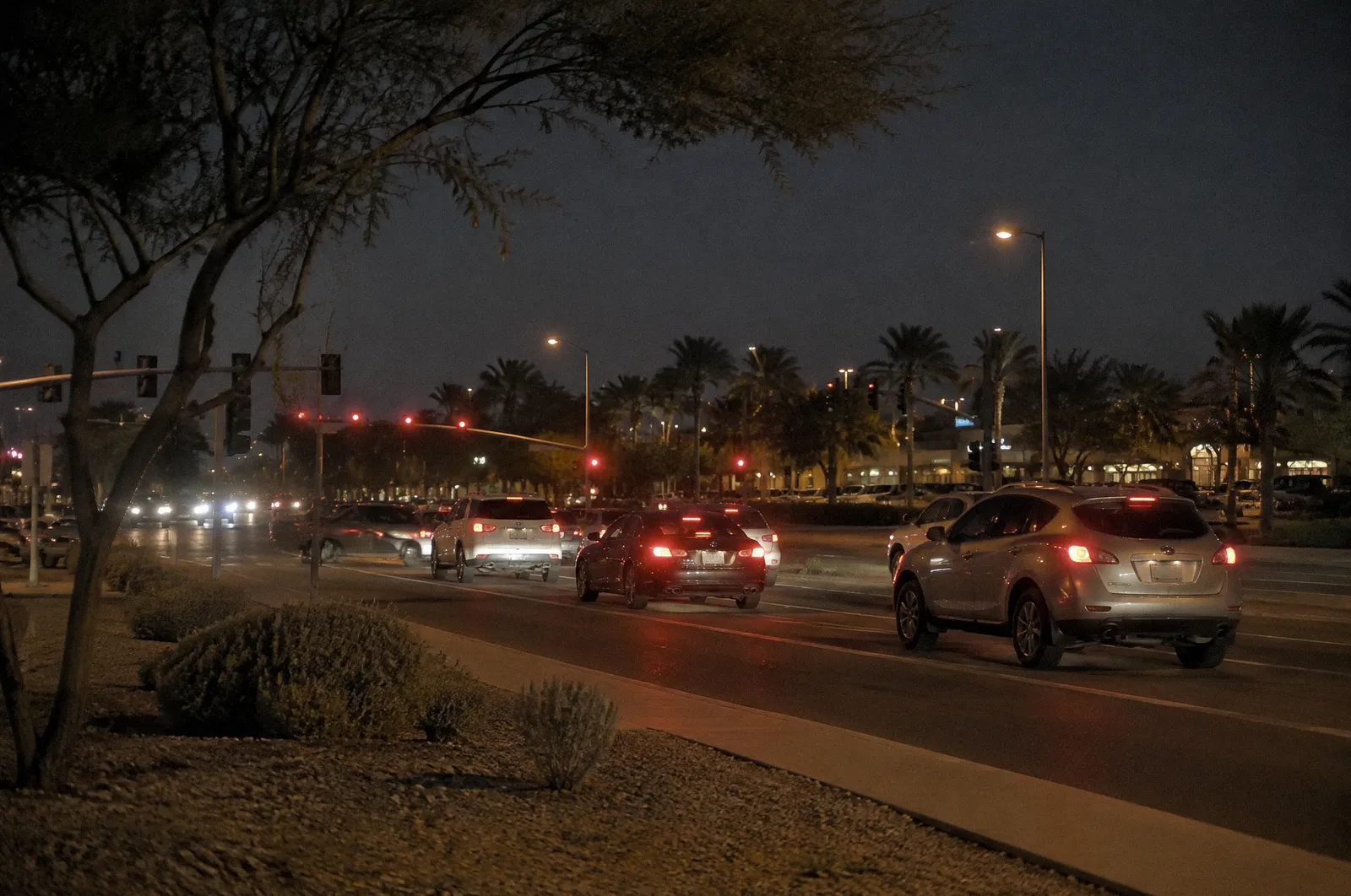 A six-lane suburban arterial in Chandler with landscaped medians and a shopping center far back, cars at a light
