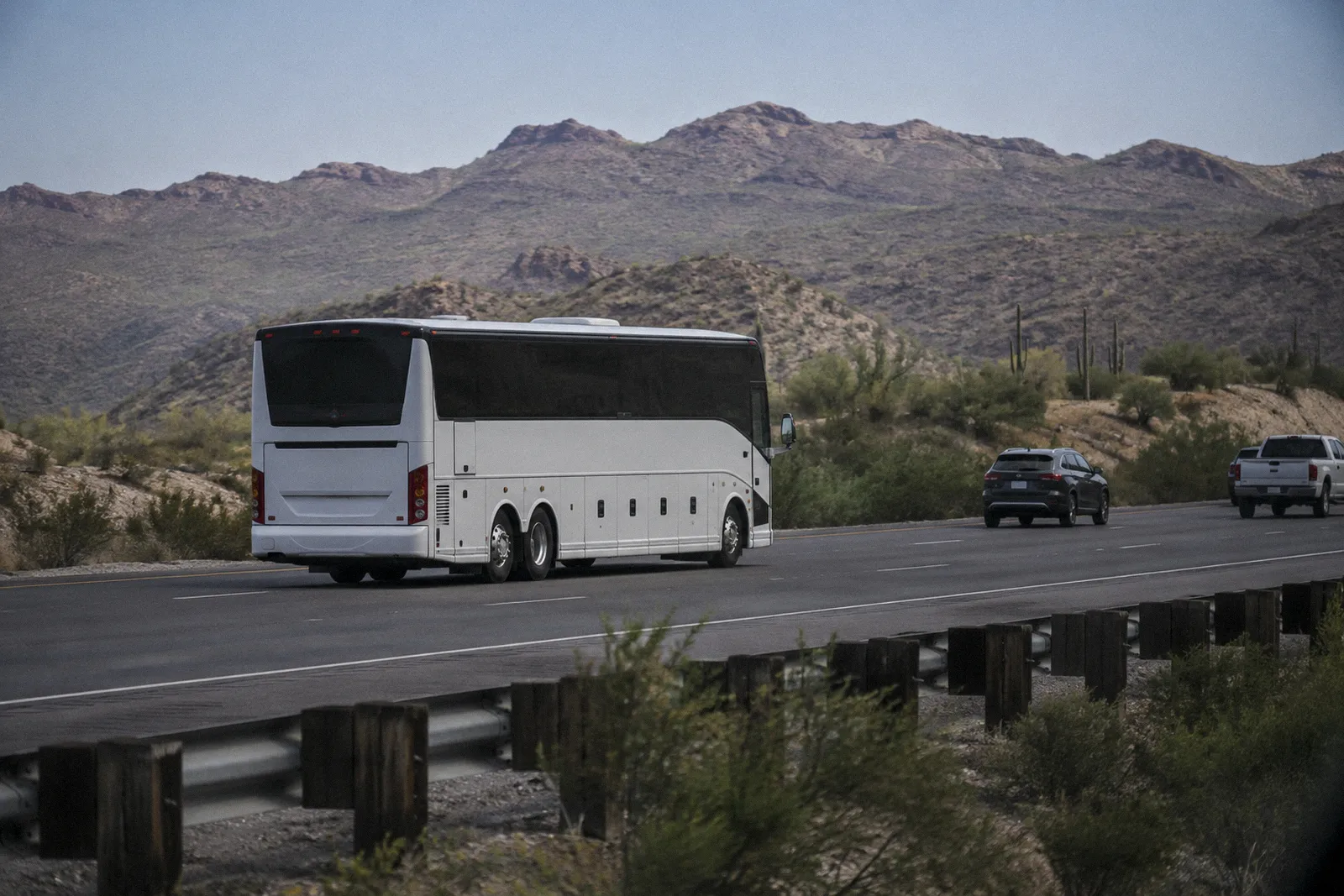 A large charter coach bus traveling on an Arizona freeway past desert hills, no readable lettering