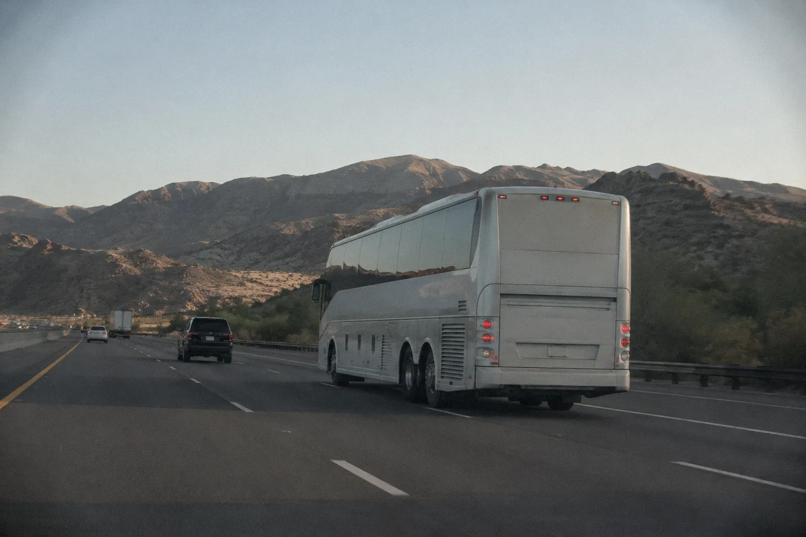 A large charter coach bus traveling on an Arizona freeway past desert hills, no readable lettering