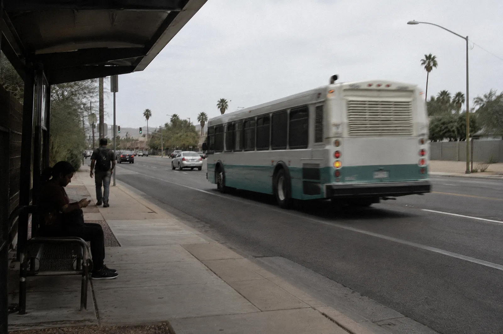 A city bus pulling away from a shaded bus stop on a Phoenix arterial, motion blur, no readable text