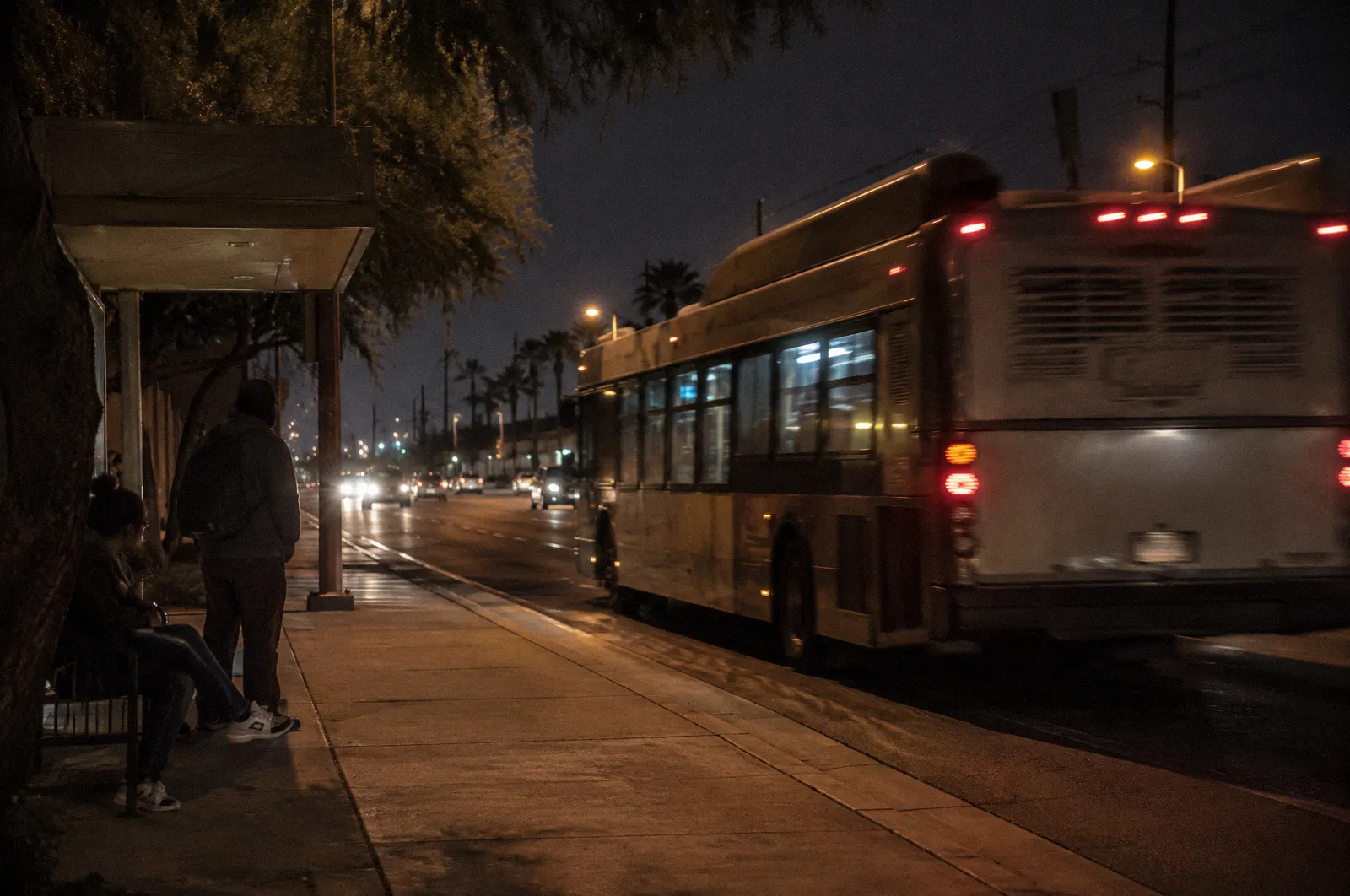 A city bus pulling away from a shaded bus stop on a Phoenix arterial, motion blur, no readable text