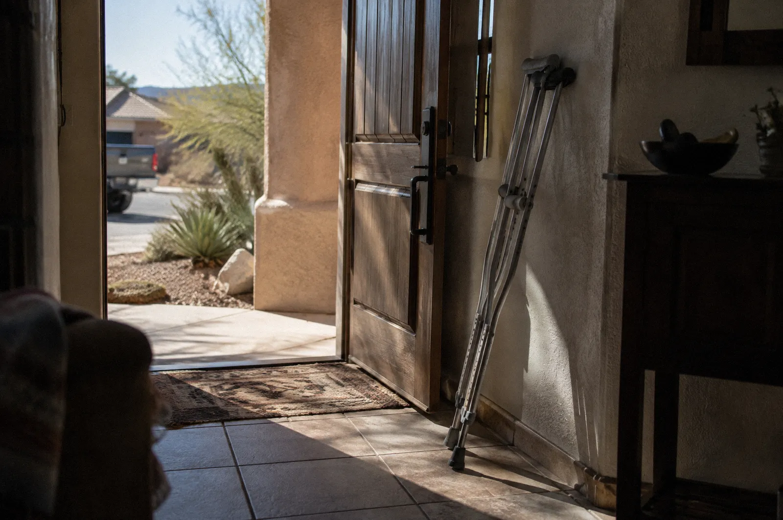 Crutches leaning by a front door of an Arizona home, sunlight across the tile floor