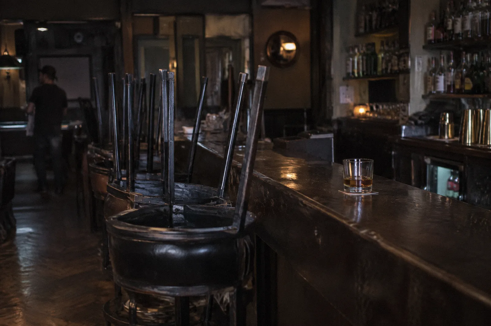 The interior of a dim bar at closing time, stools up, a single glass on the counter, no readable signs