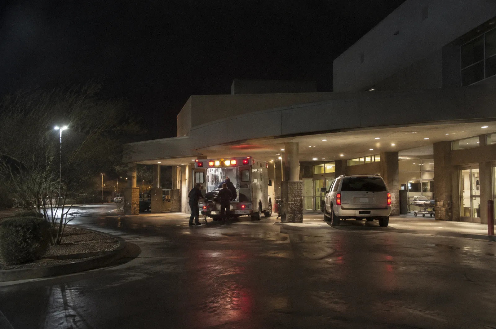 A hospital emergency entrance canopy at night, ambulance bay lights, no readable signage