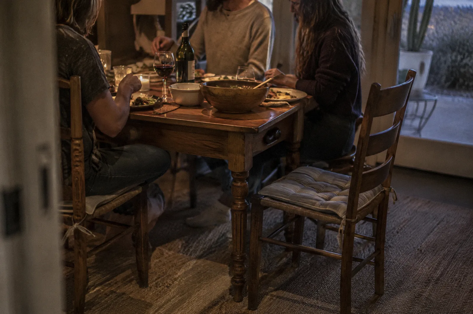 A family dinner table with one empty chair, evening light, faces out of frame
