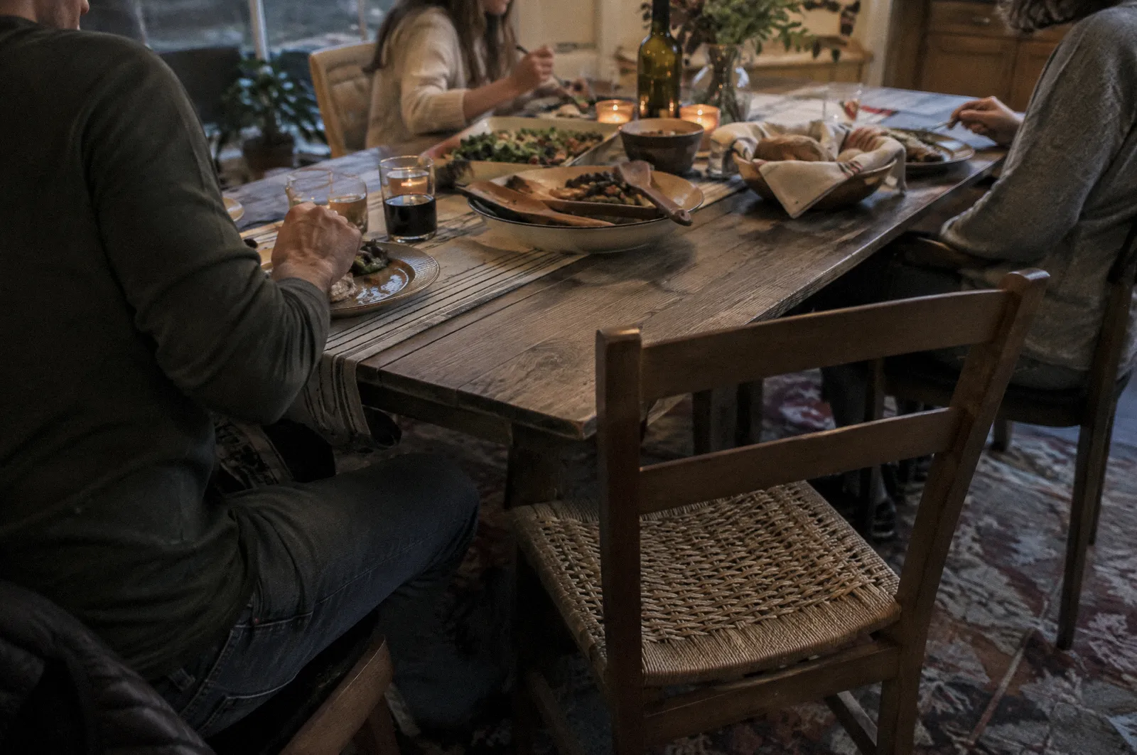 A family dinner table with one empty chair, evening light, faces out of frame