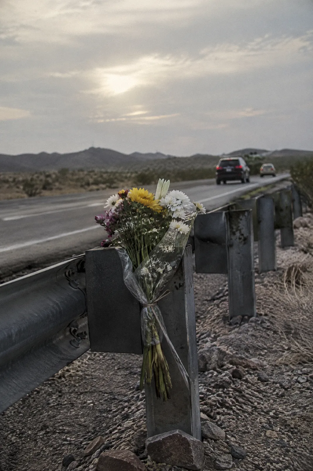 A small roadside memorial of fresh flowers tied to a guardrail on a desert highway