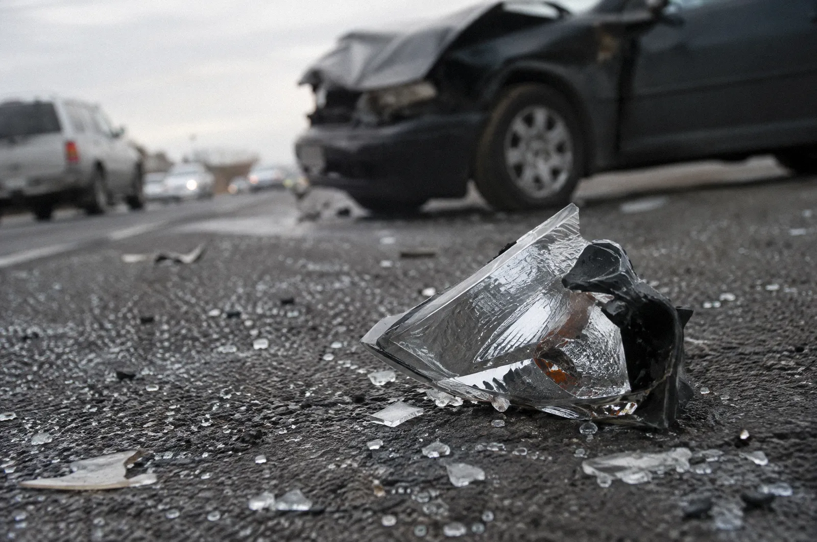 Shattered safety glass and a broken headlight fragment on dark asphalt, shallow depth of field