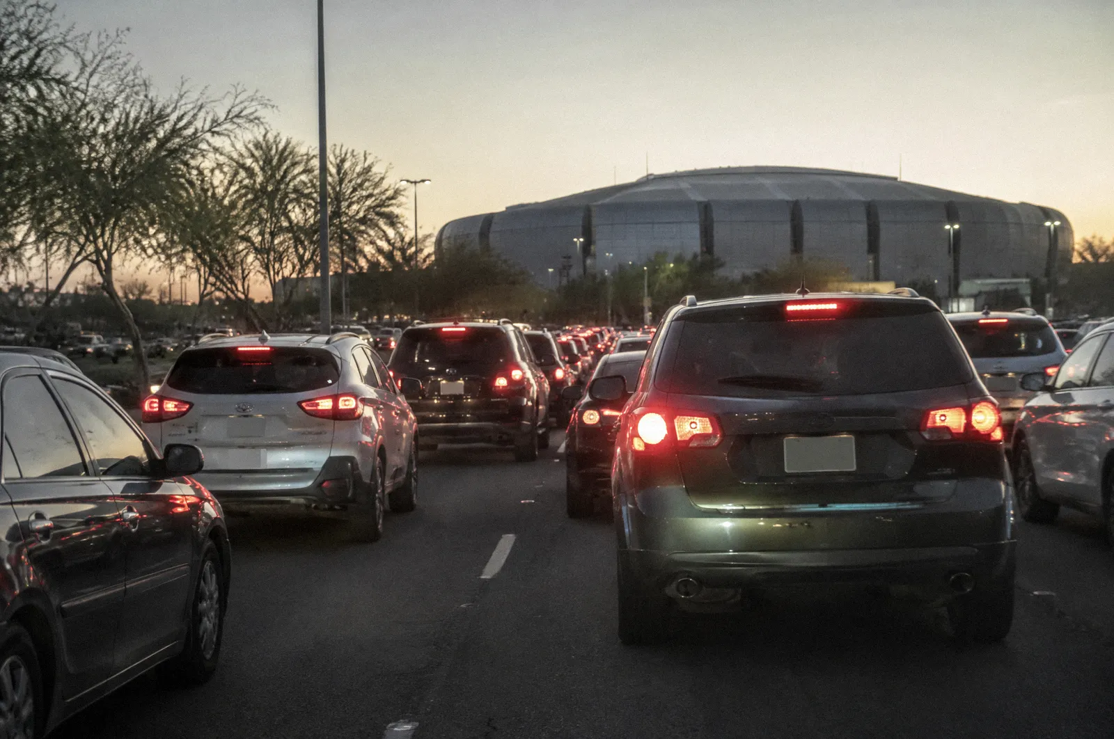 Heavy evening event traffic on a Glendale arterial near a large stadium silhouette, brake lights glowing