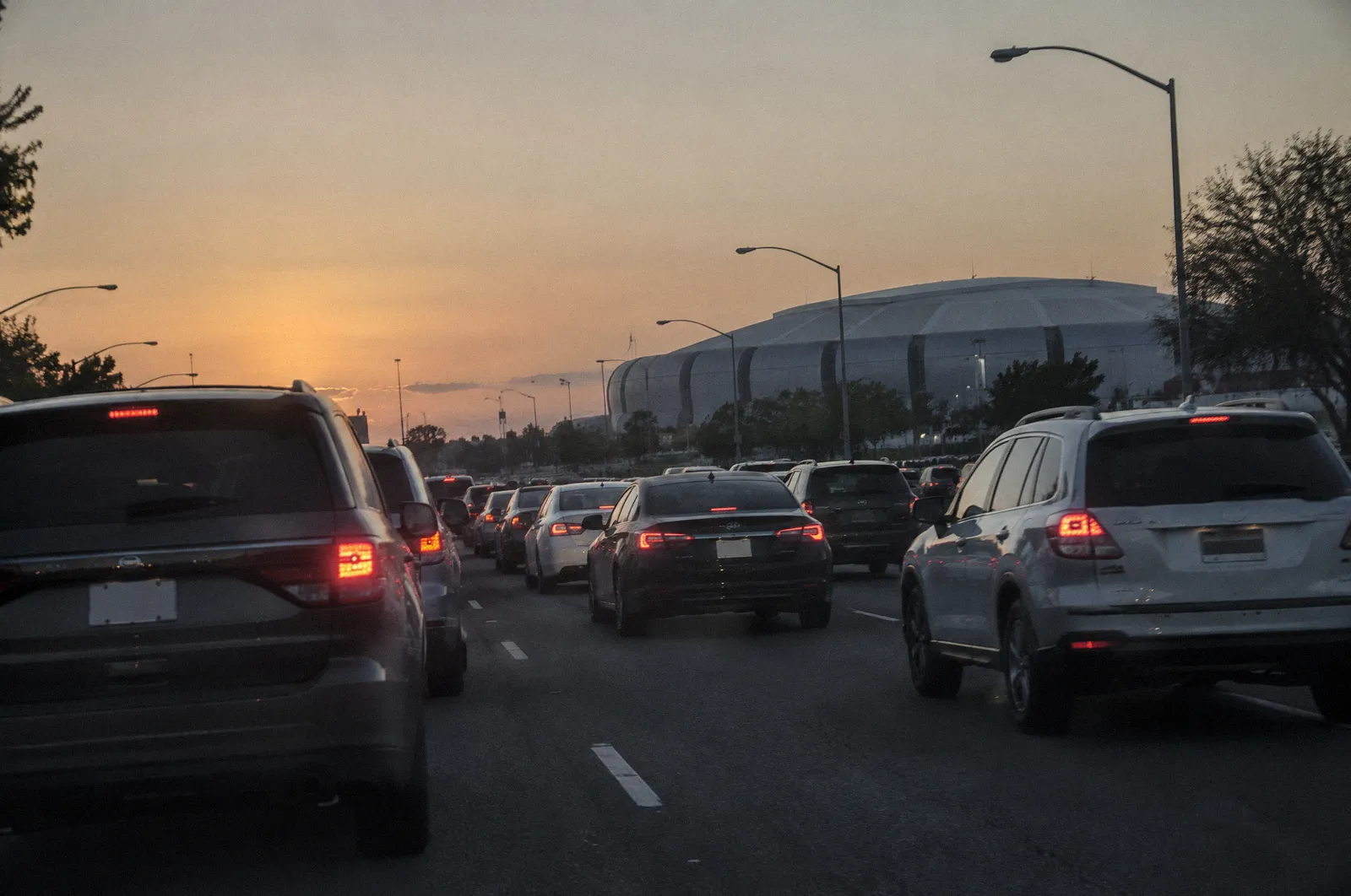 Heavy evening event traffic on a Glendale arterial near a large stadium silhouette, brake lights glowing