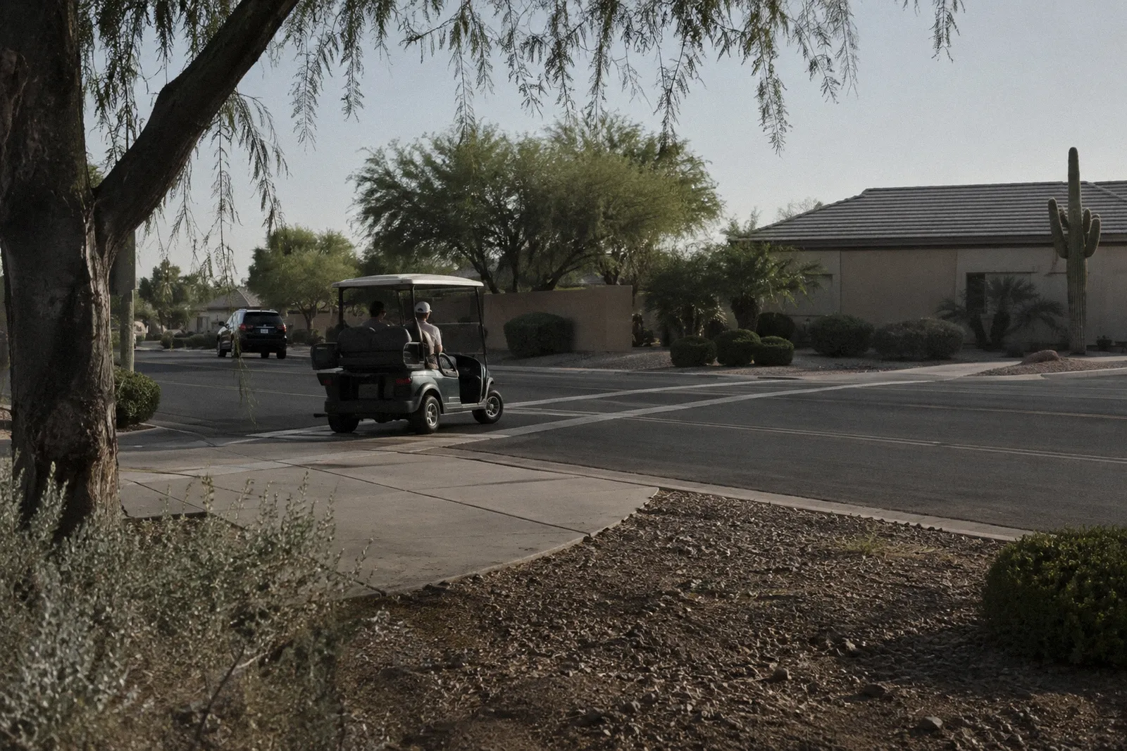 A golf cart path crossing a two-lane neighborhood road, painted crossing lines, a cart waiting to cross