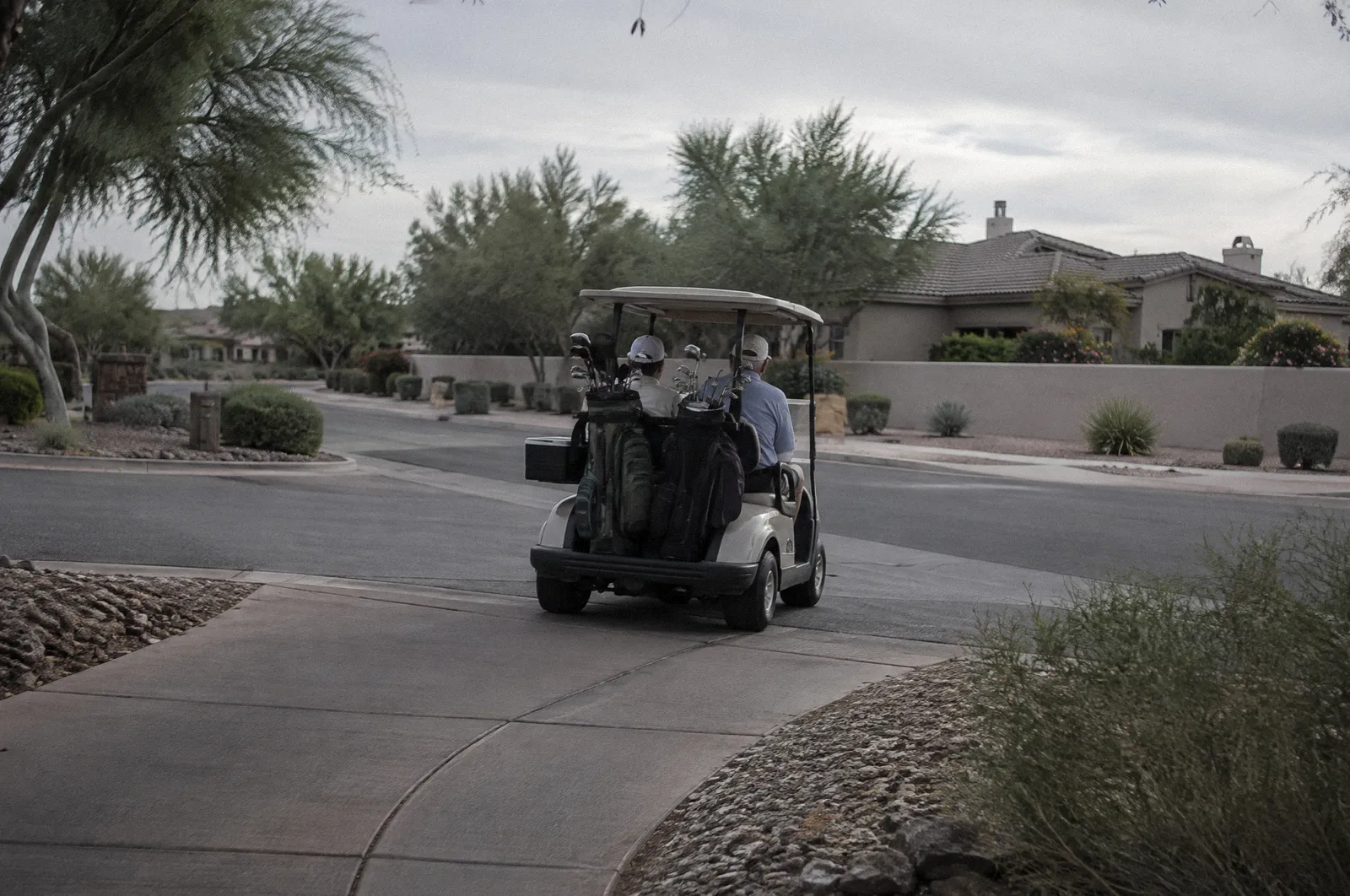 A golf cart on a cart path crossing a neighborhood street in a Scottsdale community, afternoon