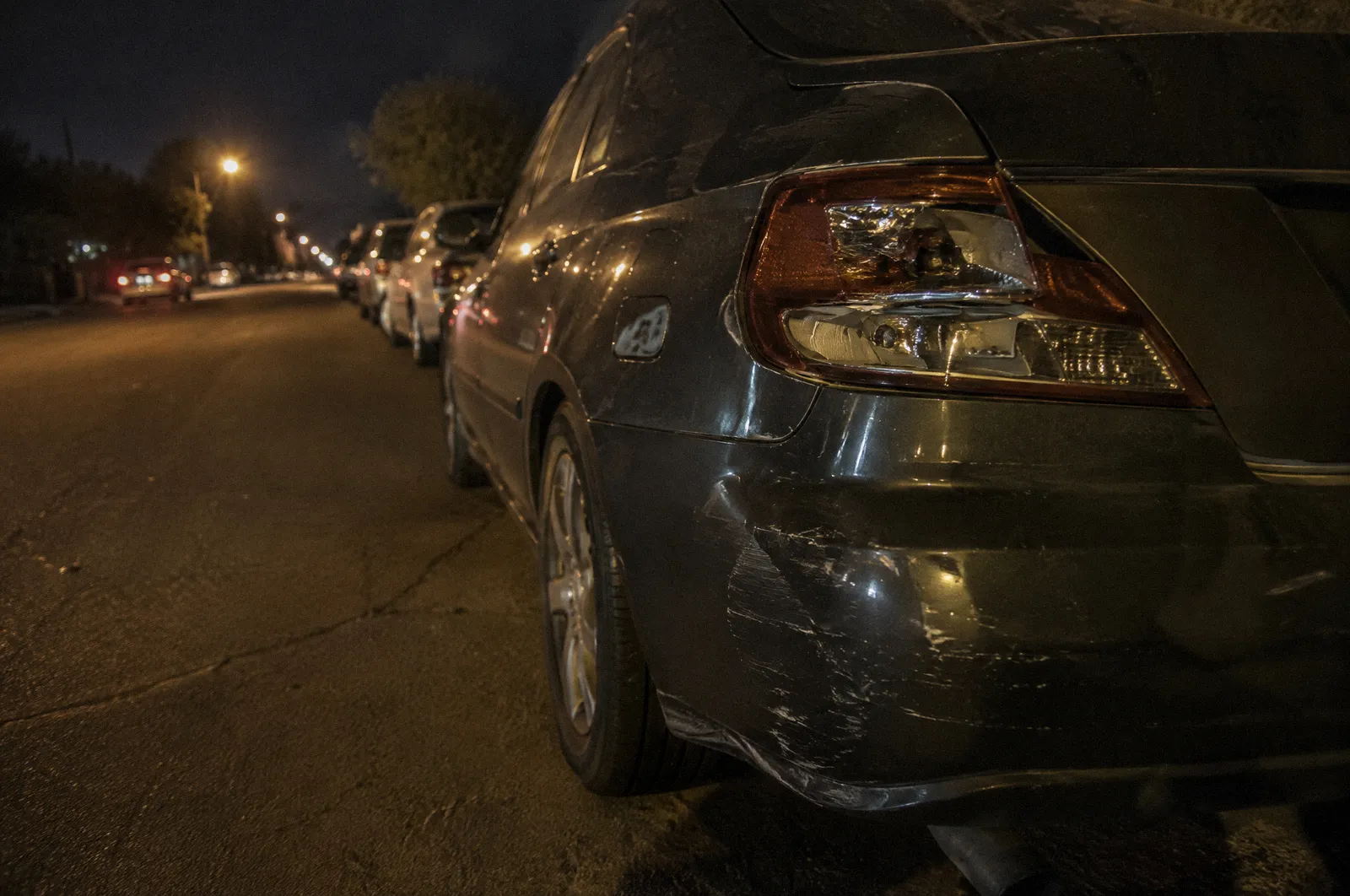A broken taillight and scraped paint on a parked car at night, streetlight glare