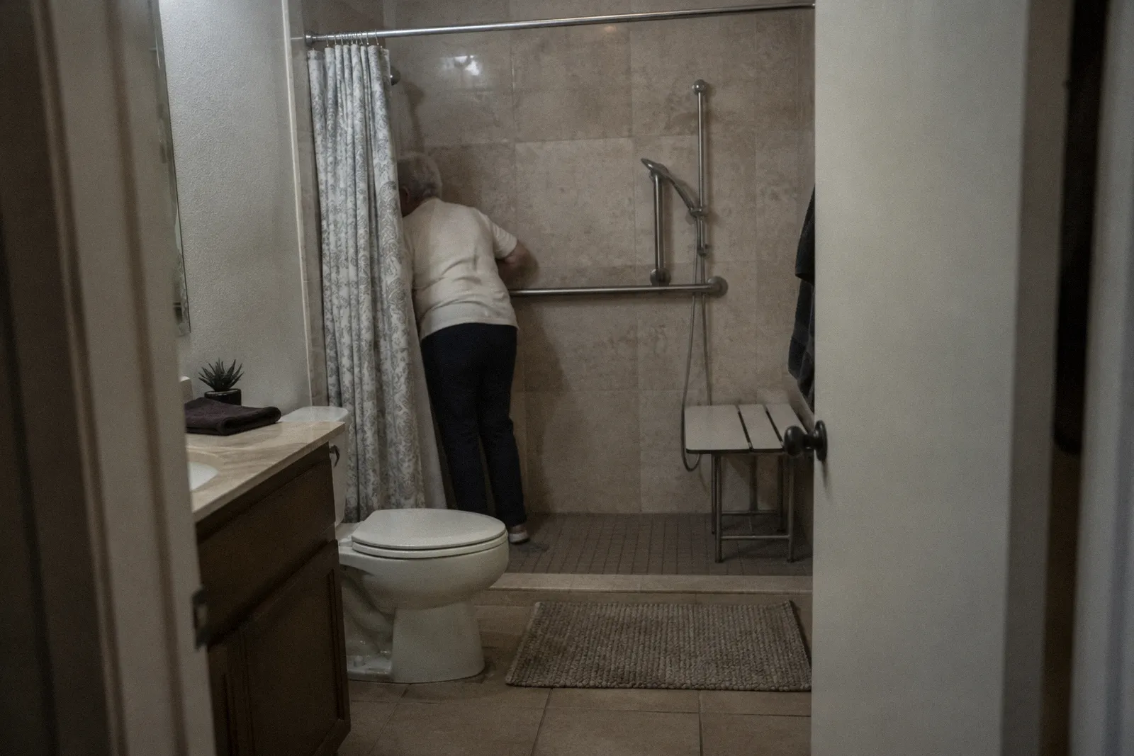 A home bathroom modified with grab bars and a roll-in shower, clean and plain