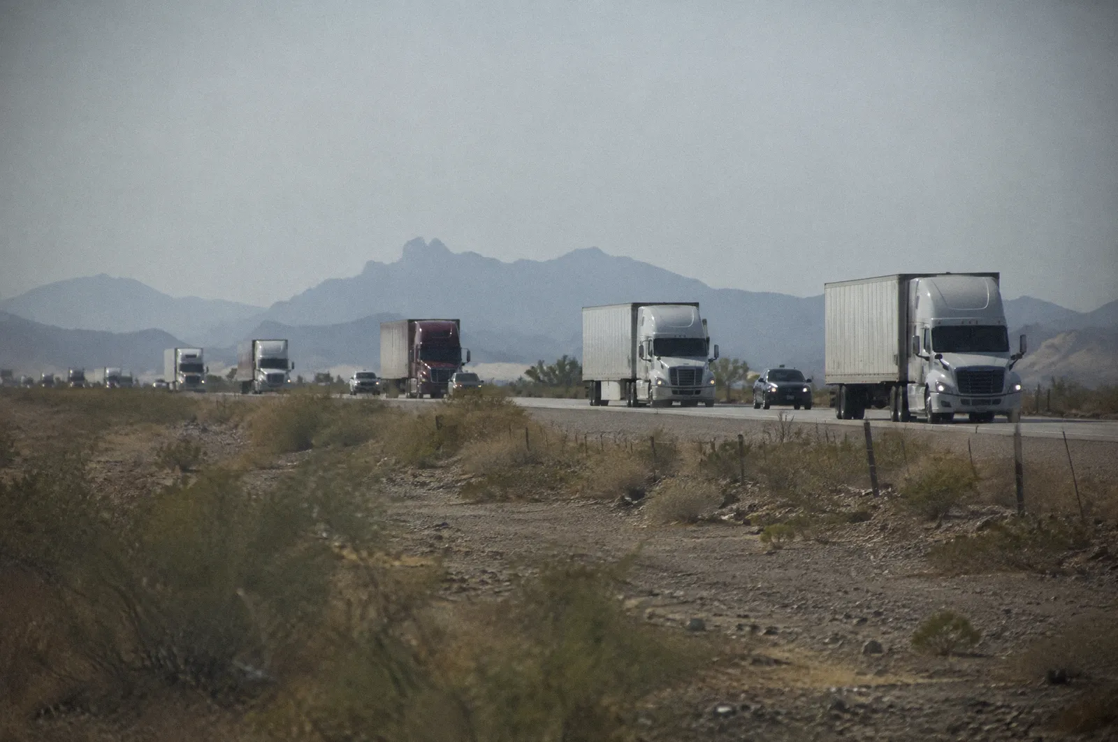 A line of semi trucks on Interstate 10 west of Phoenix, flat desert, long telephoto compression