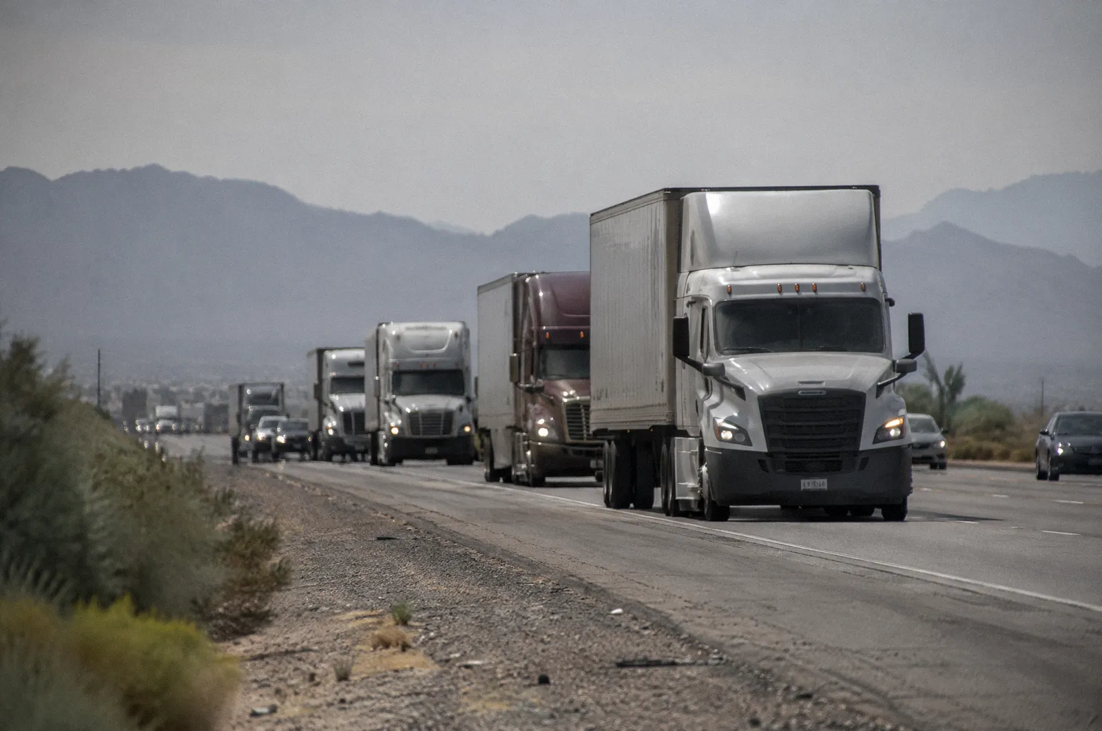 A line of semi trucks on Interstate 10 west of Phoenix, flat desert, long telephoto compression