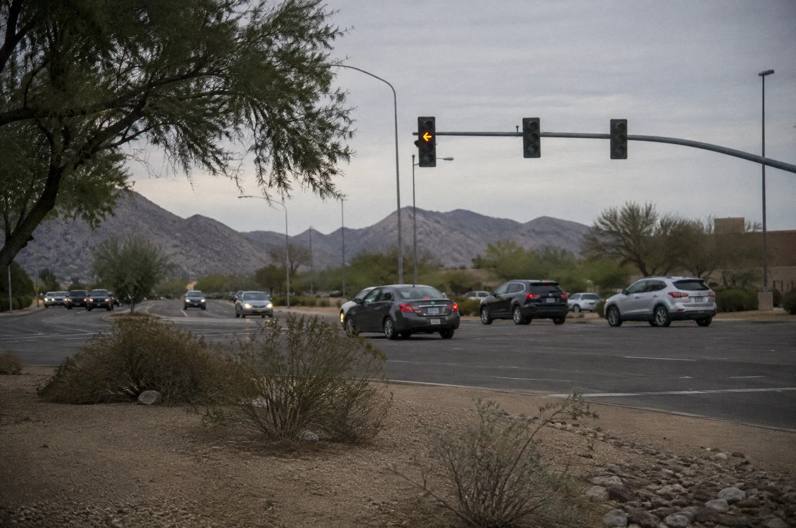 A car waiting to turn left across oncoming traffic at a desert suburban intersection, flashing yellow arrow