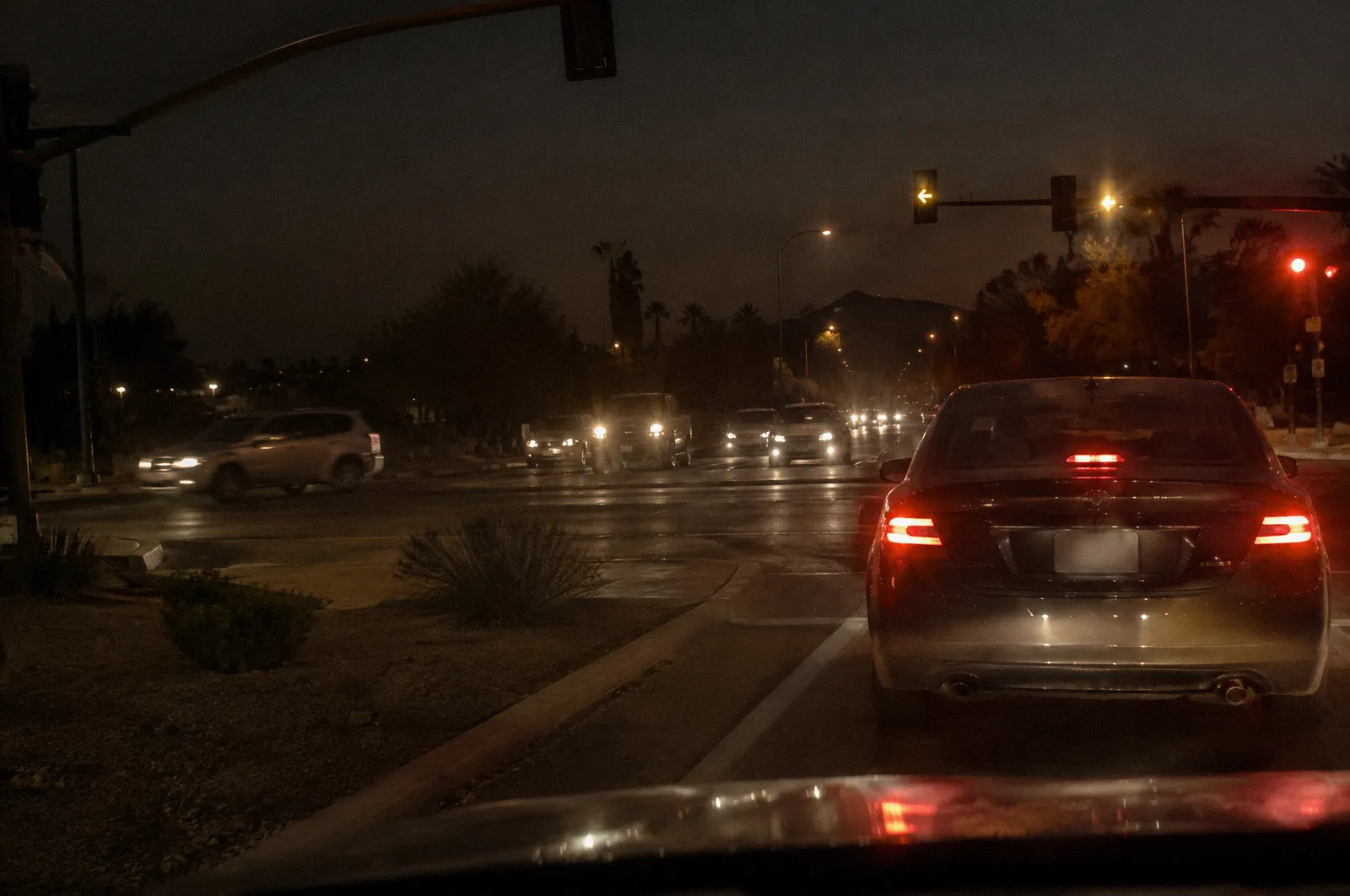 A car waiting to turn left across oncoming traffic at a desert suburban intersection, flashing yellow arrow