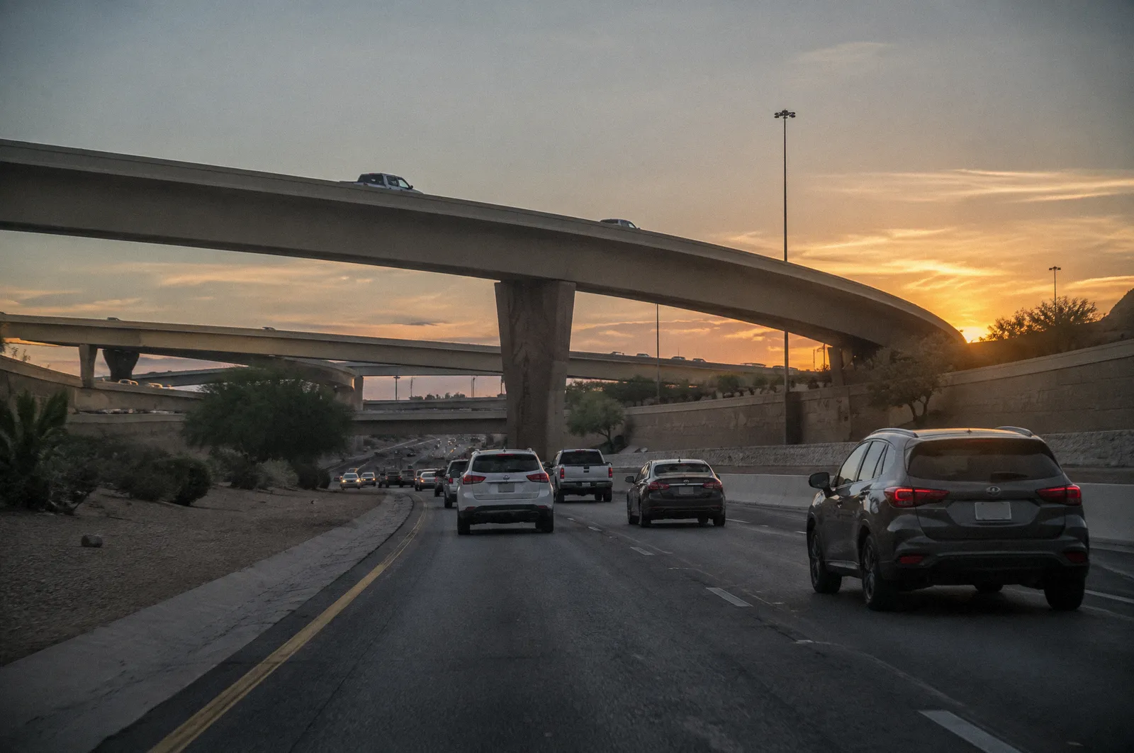 A Loop 101 freeway overpass at sunset, layered ramps, cars streaming, desert-colored sound walls