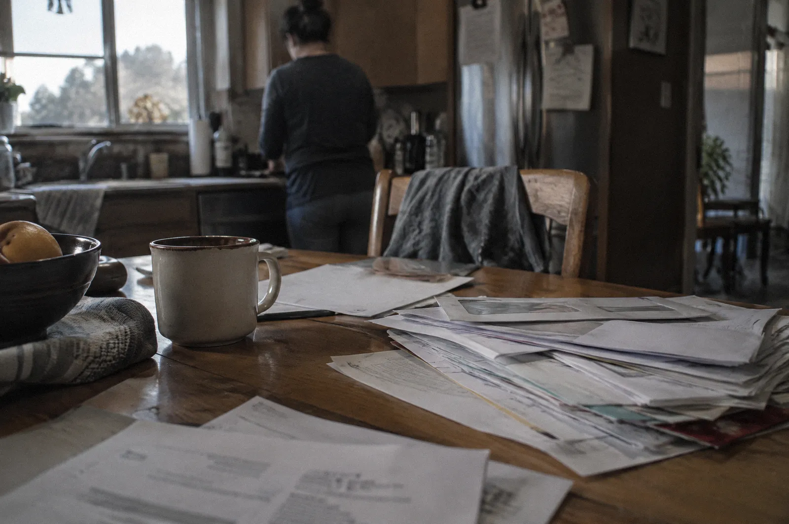 A stack of hospital bills and envelopes on a kitchen table, all text blurred and unreadable, coffee mug