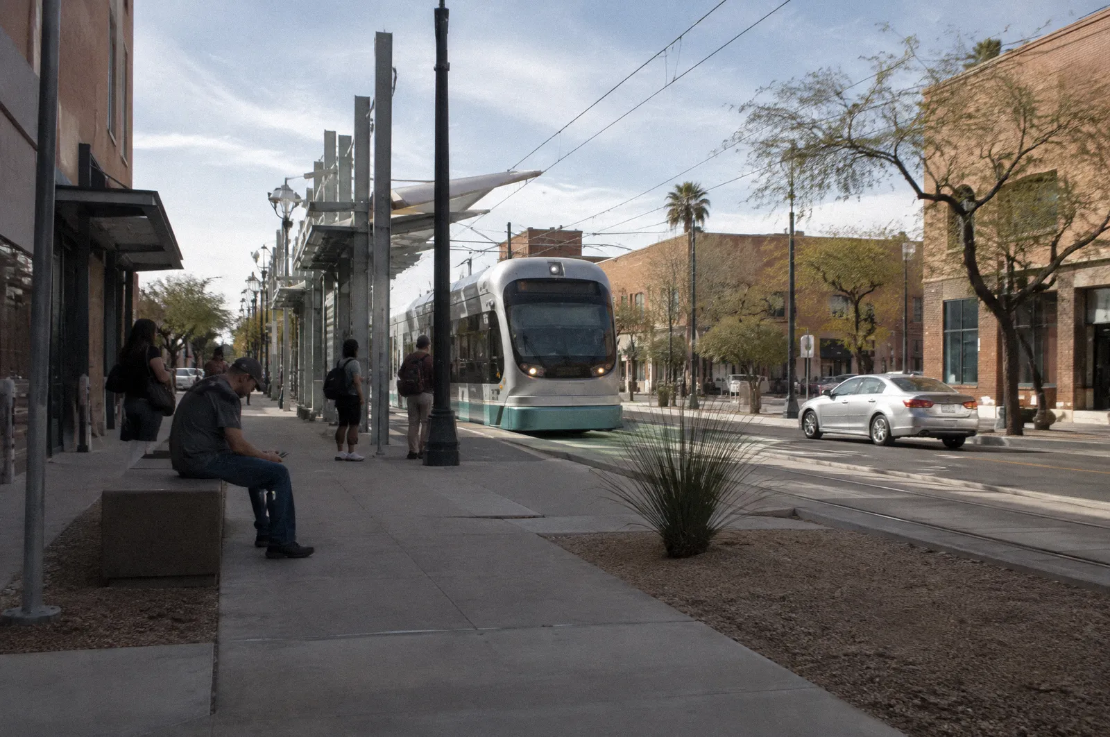 A downtown Mesa street with low brick buildings, wide sidewalks, light rail stop, midday