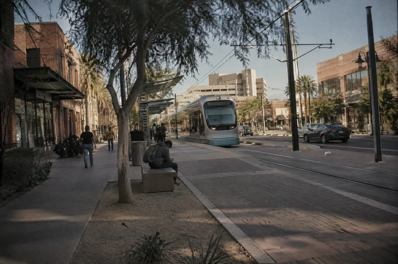 A downtown Mesa street with low brick buildings, wide sidewalks, light rail stop, midday