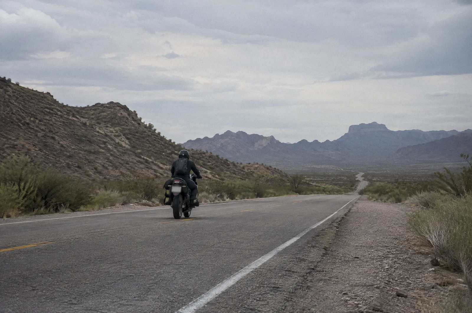 A motorcycle rider from behind on an empty desert highway, helmet and jacket, heat shimmer