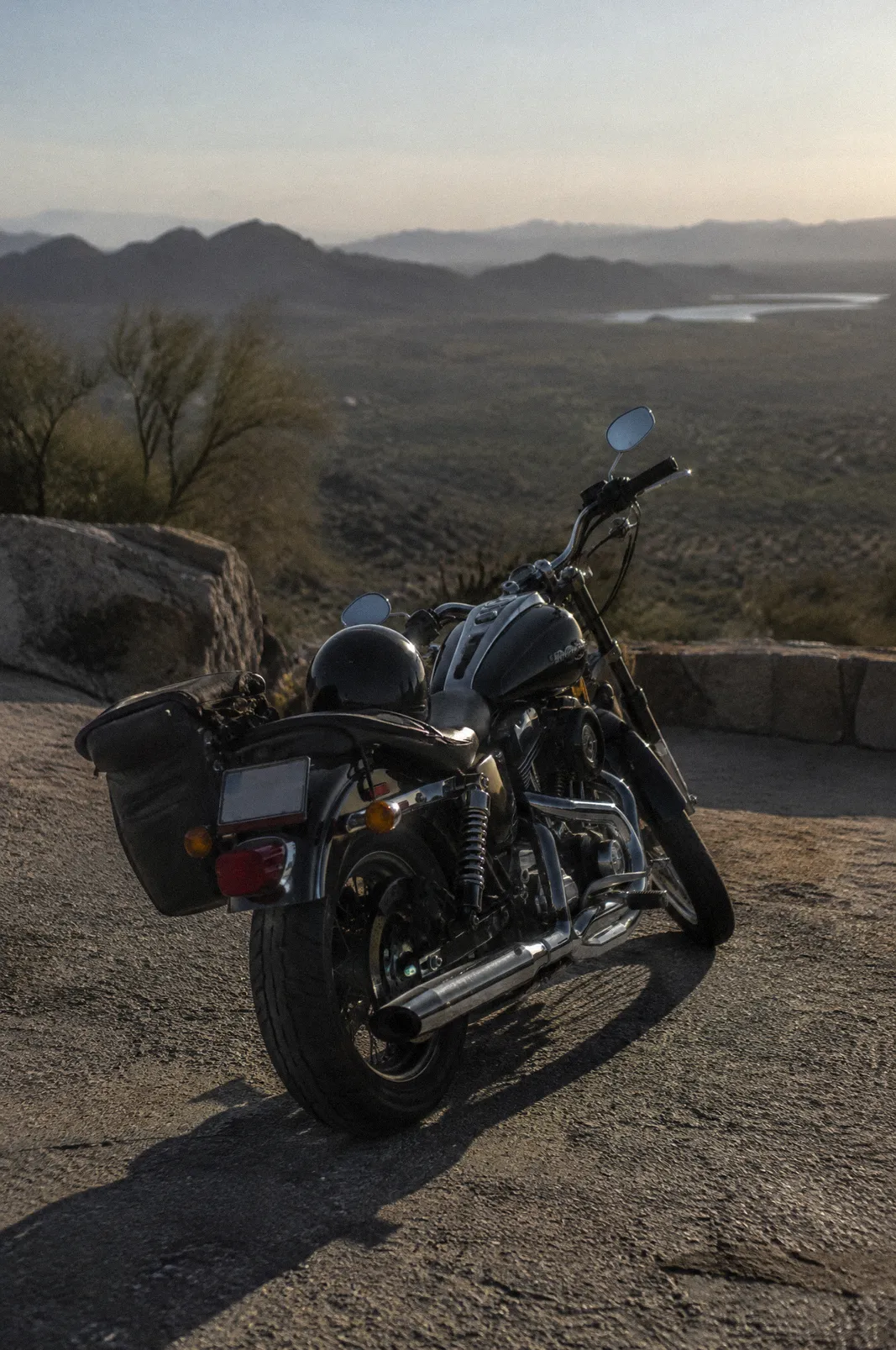 A cruiser motorcycle parked at a desert overlook, helmet on the seat, late afternoon