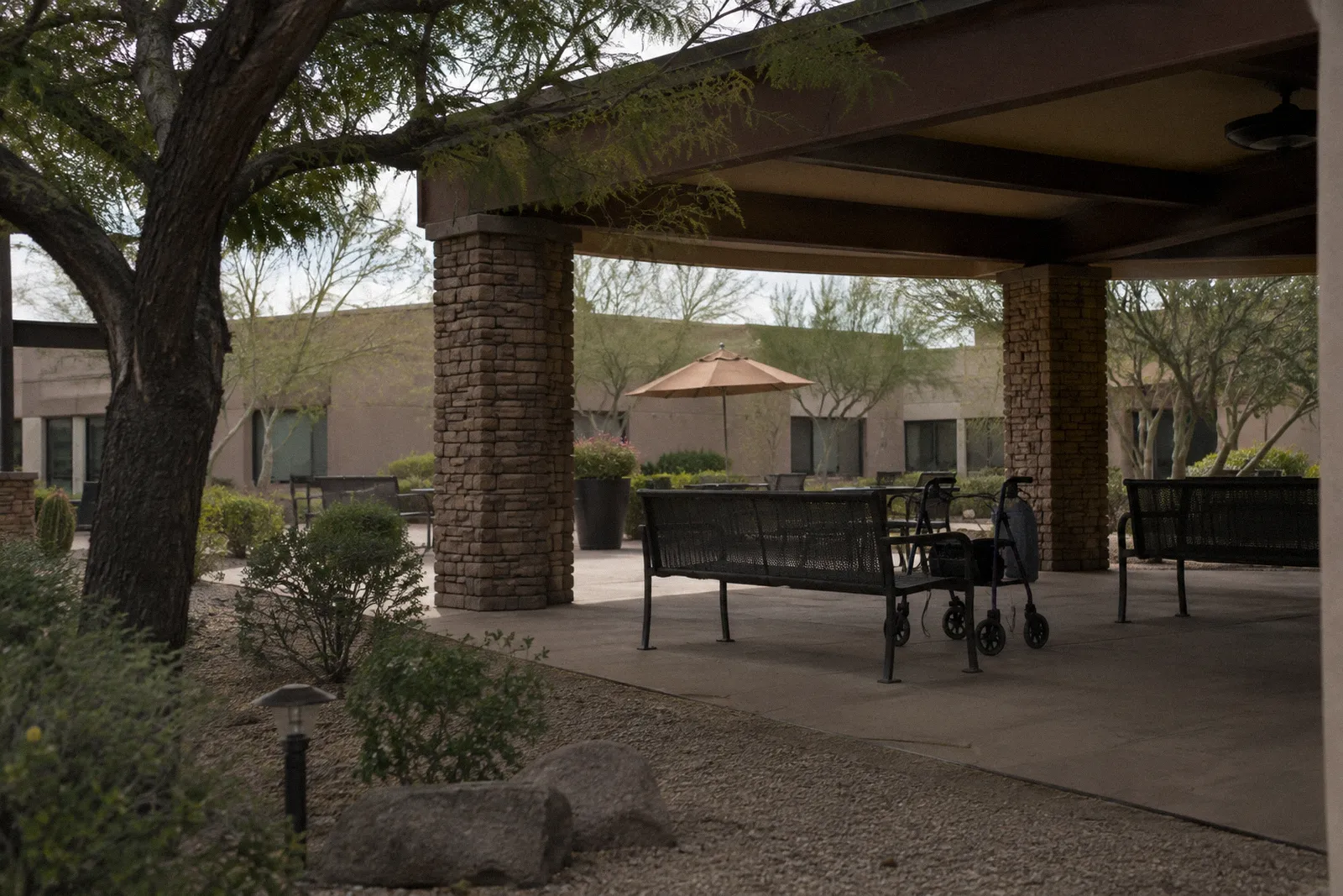 The courtyard garden of a senior care facility in Arizona with shaded benches, a walker beside a bench, no people