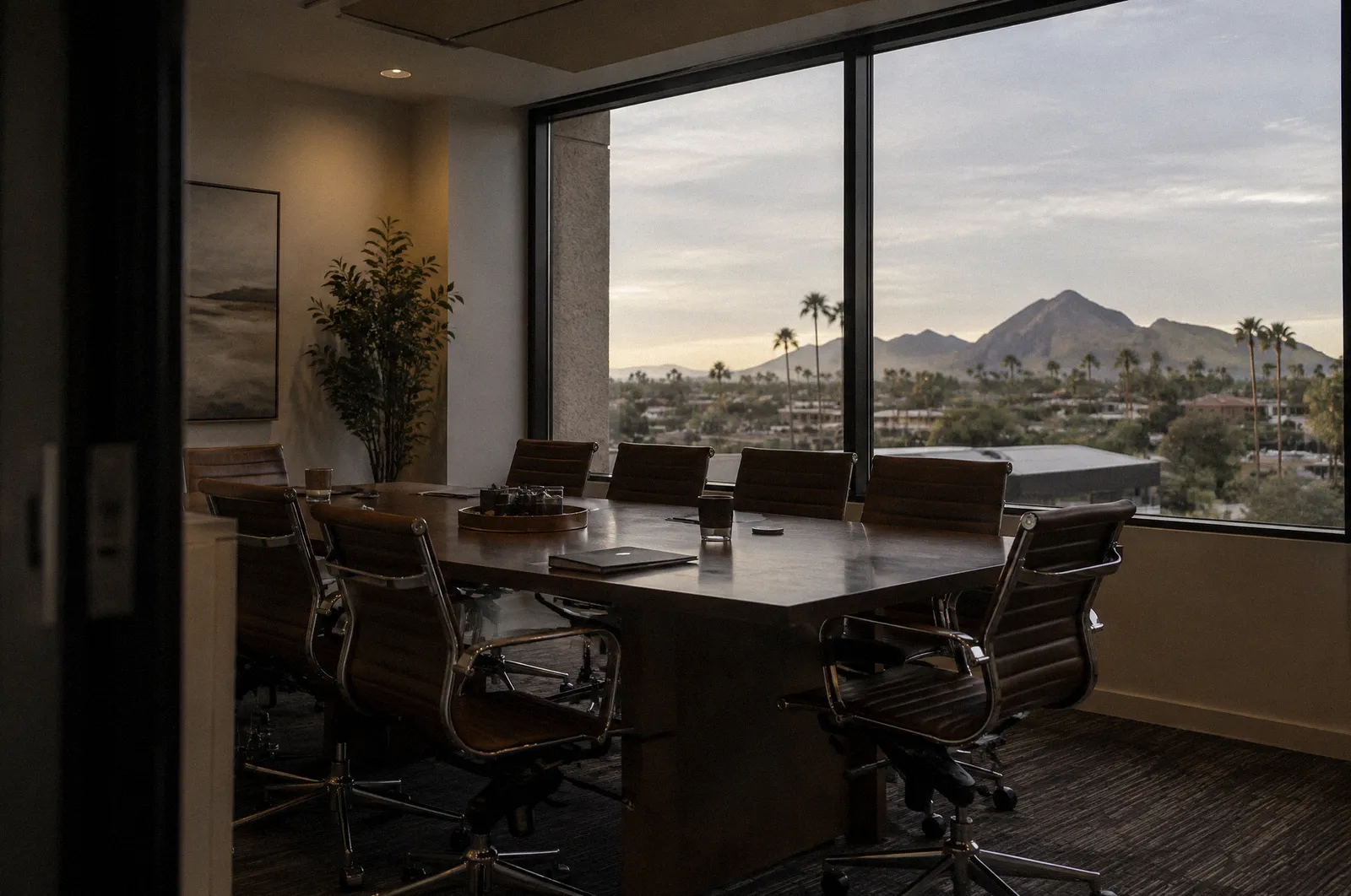 A law office conference room with a window view of Scottsdale palms and mountains, empty chairs, late light