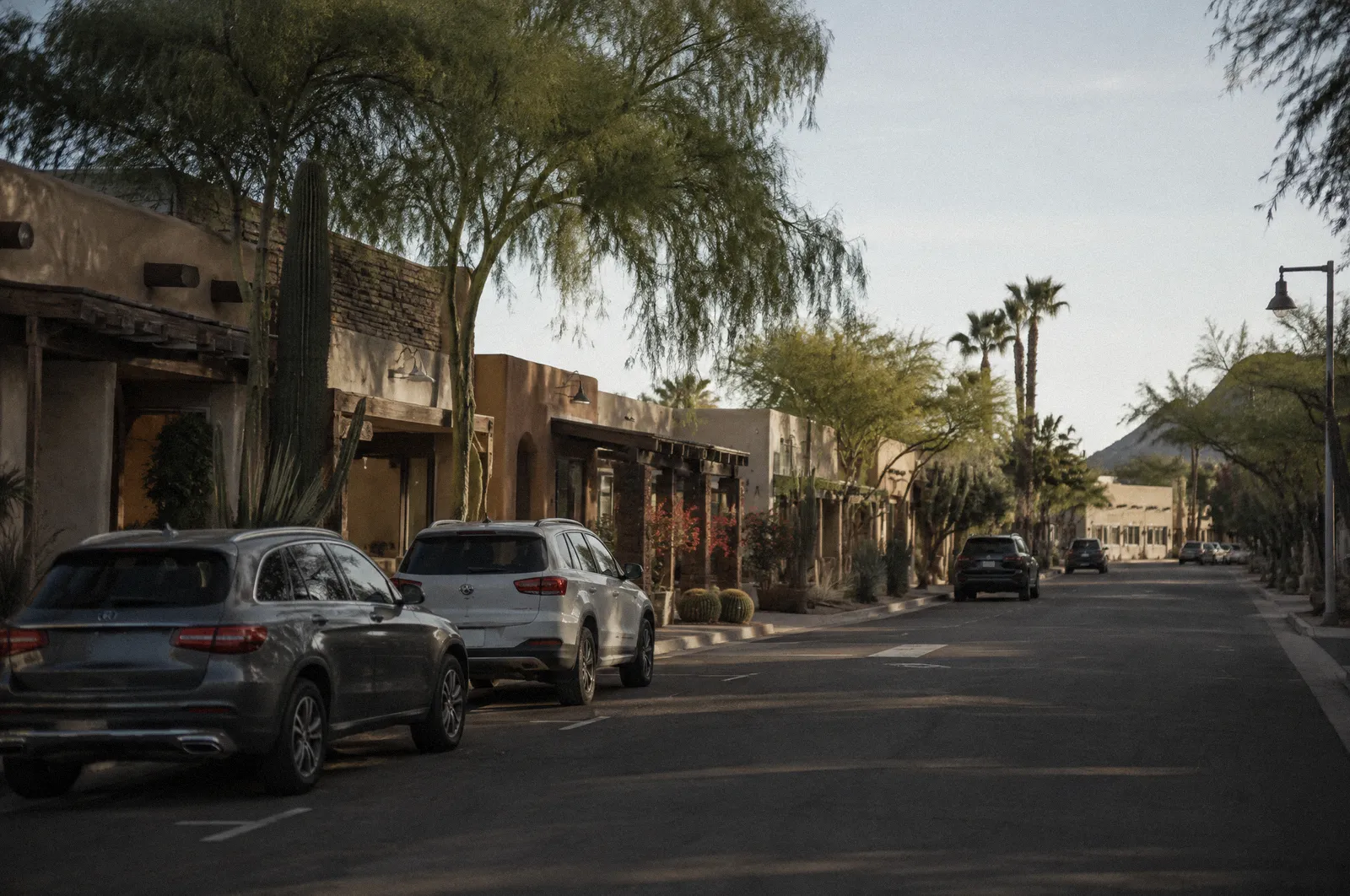 An empty Old Town Scottsdale side street early morning, low adobe-style storefronts with blank facades, desert landscaping, parked cars