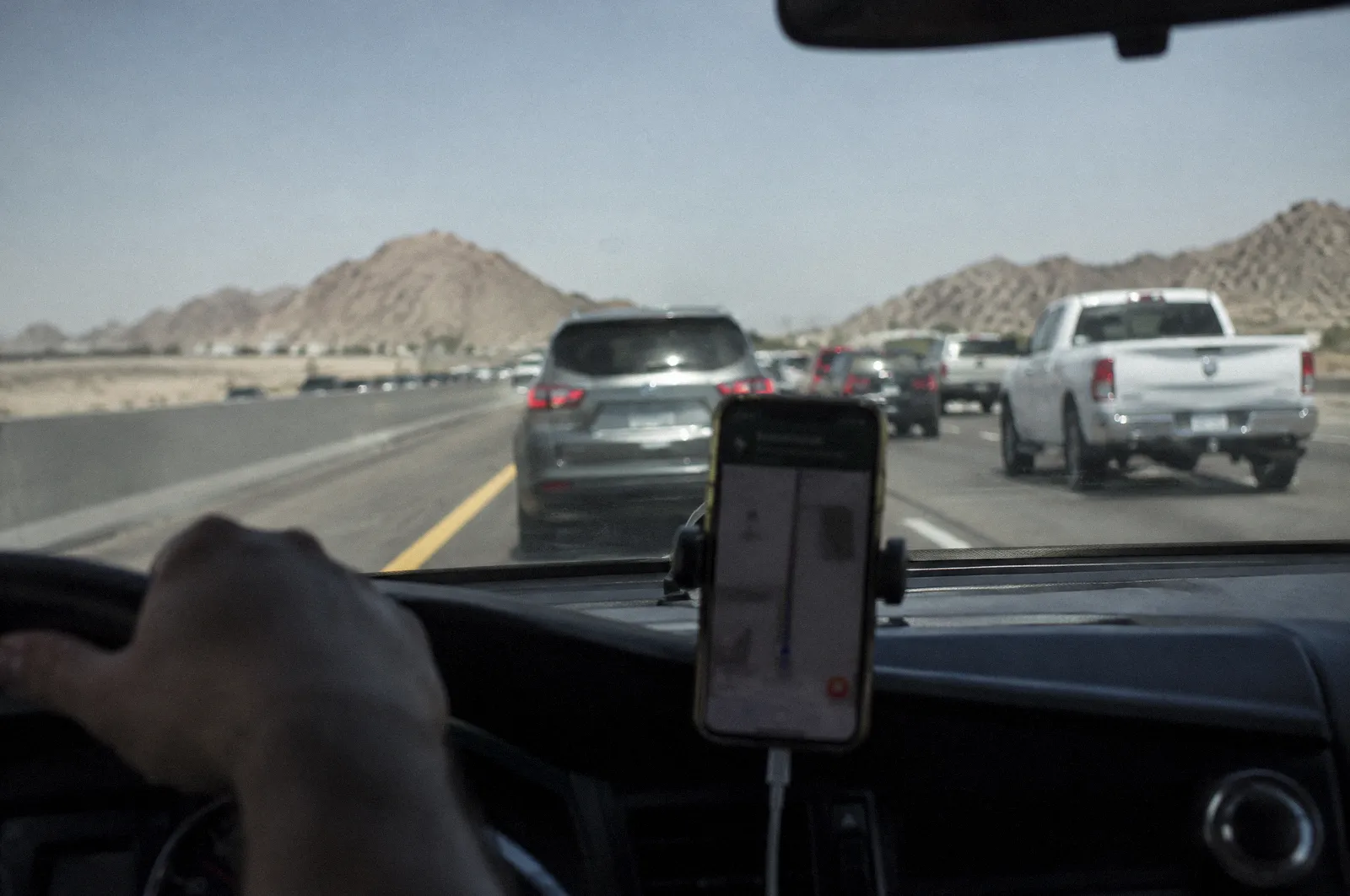 A phone in a dashboard mount showing a blurred screen, the windshield view of traffic ahead out of focus