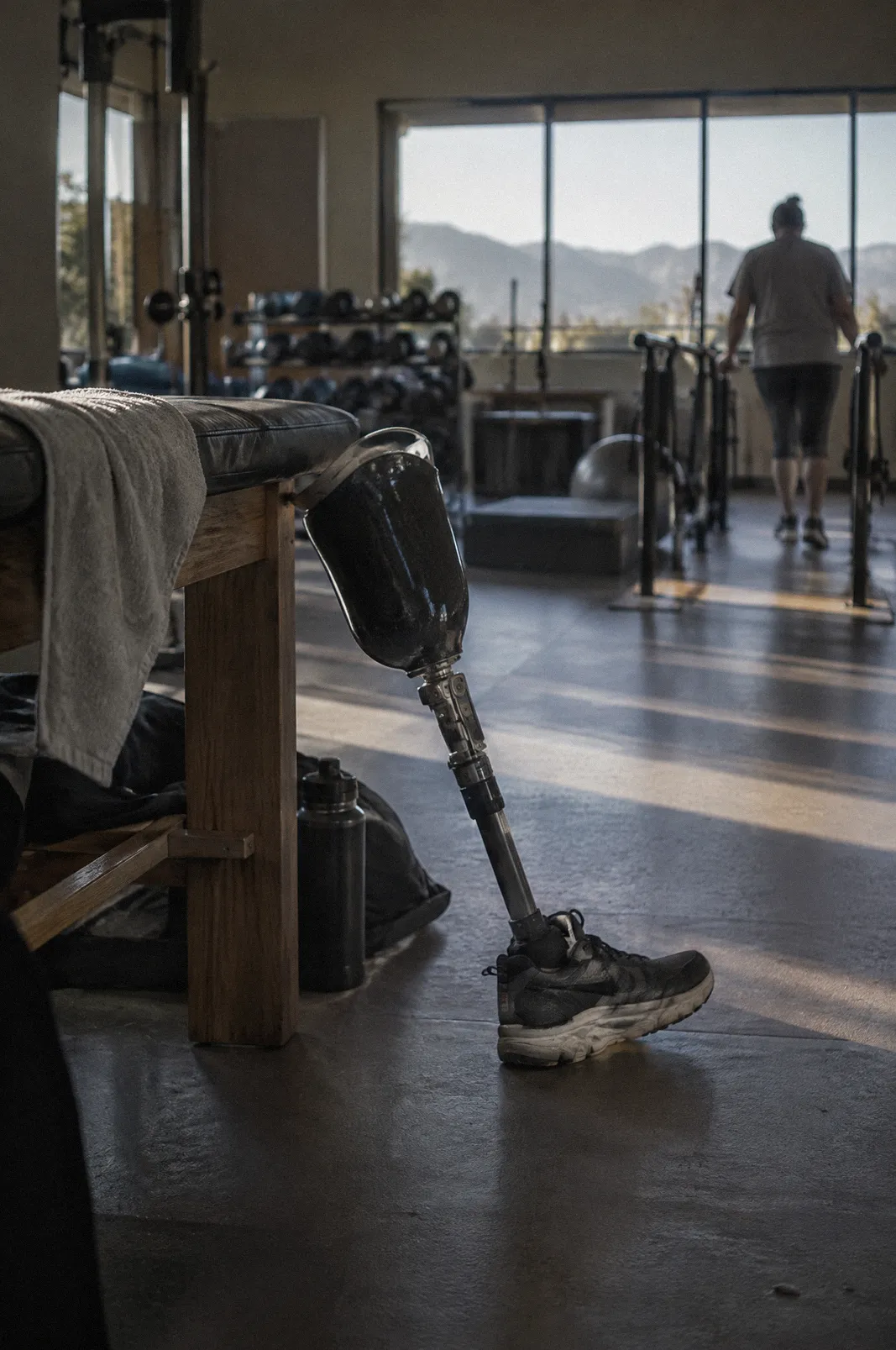 A prosthetic leg leaning against a bench in a rehab gym, morning window light