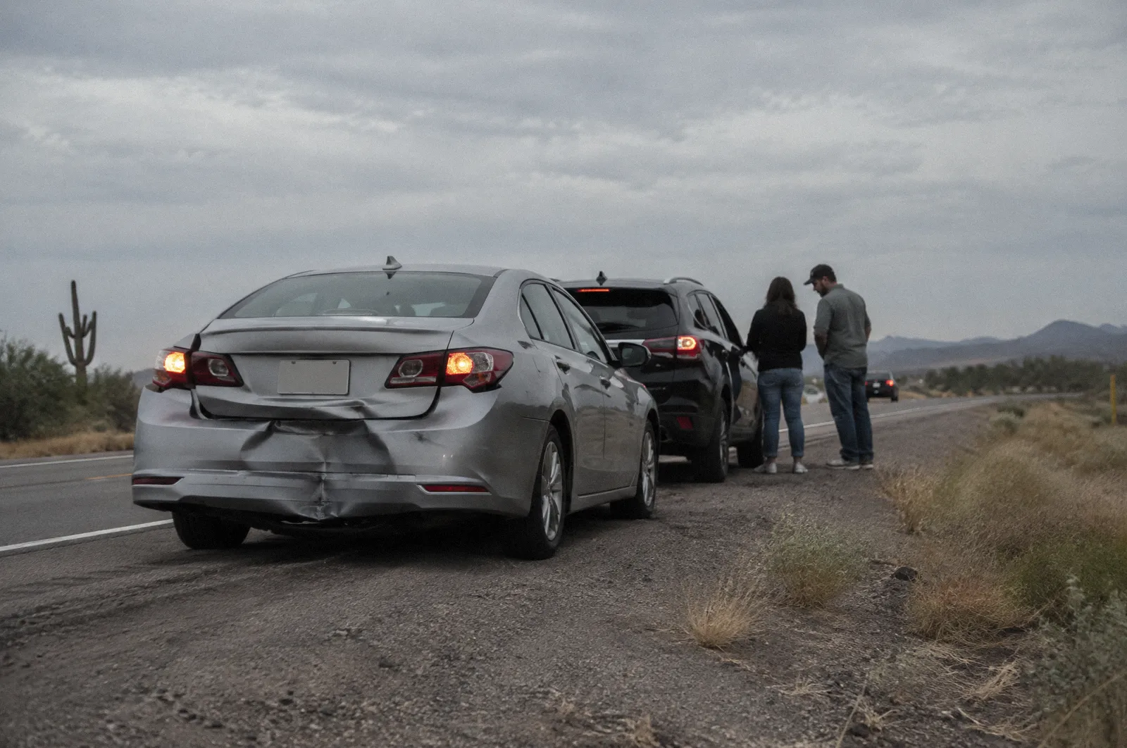 Two cars stopped on a road shoulder after a low-speed rear-end collision, crumpled rear bumper, hazard lights on