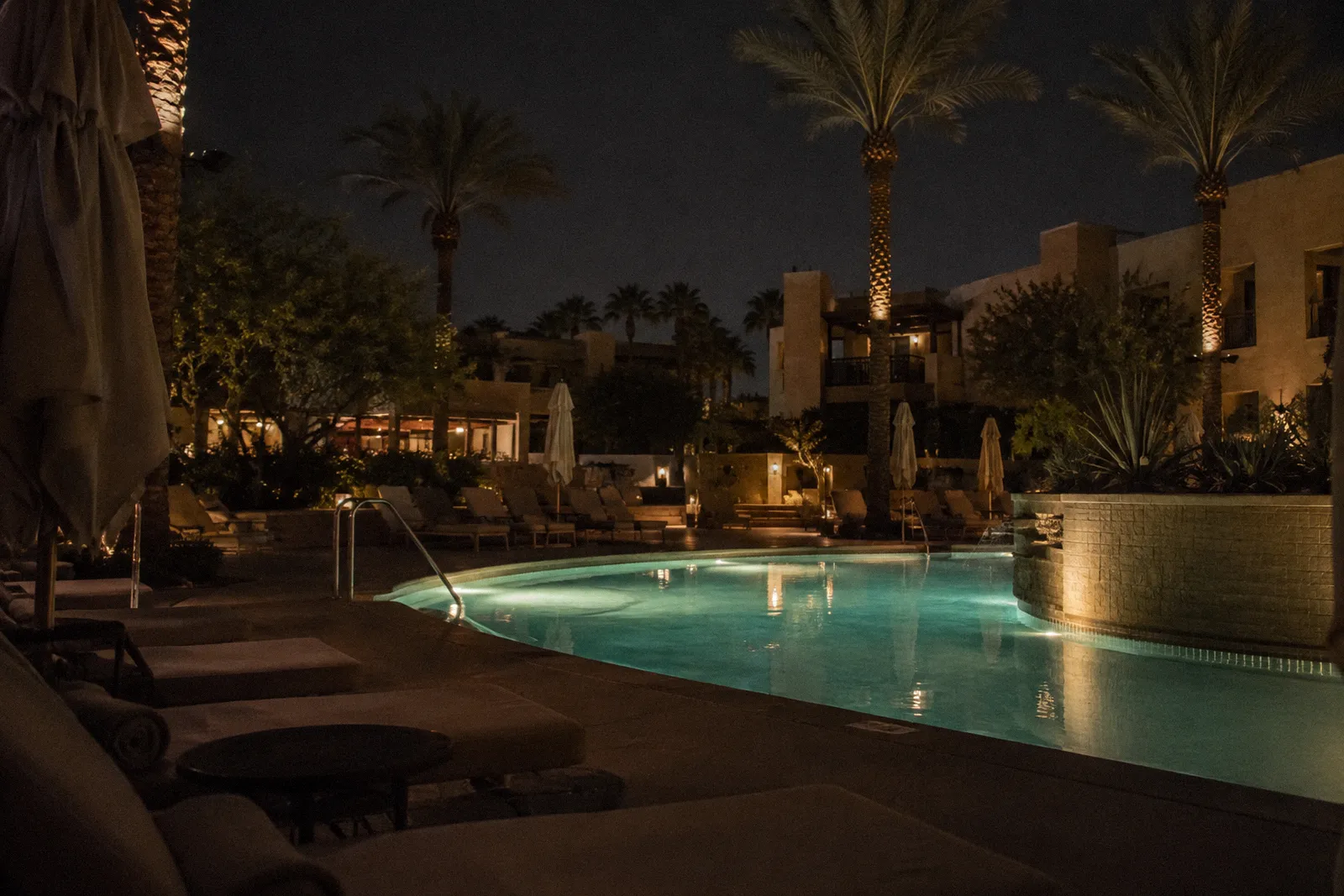 A quiet Scottsdale resort pool with rows of empty lounge chairs and umbrellas, palms, no people