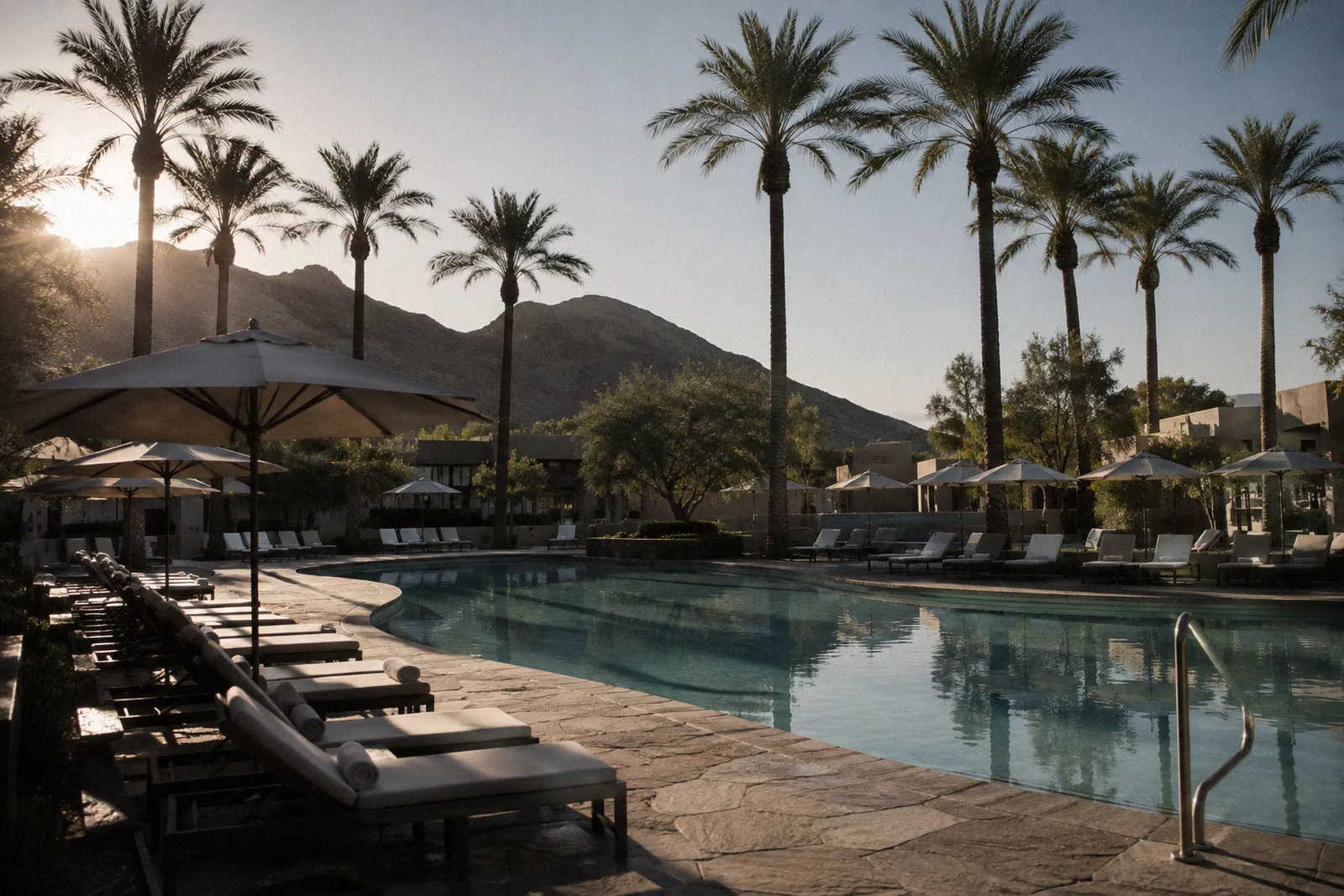 A quiet Scottsdale resort pool with rows of empty lounge chairs and umbrellas, palms, no people