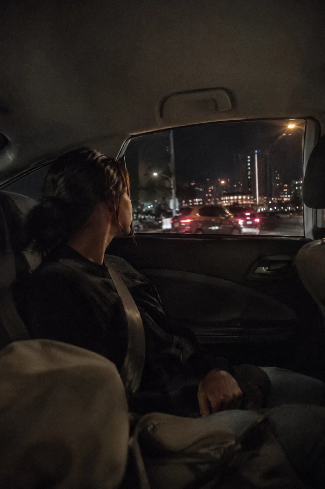 The back seat of a sedan at night from the passenger side, city lights through the window, seatbelt
