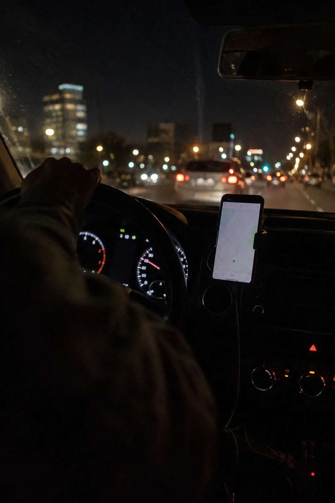 A phone in a dashboard mount showing a blank map screen inside a car at night, city lights through the windshield, no readable text