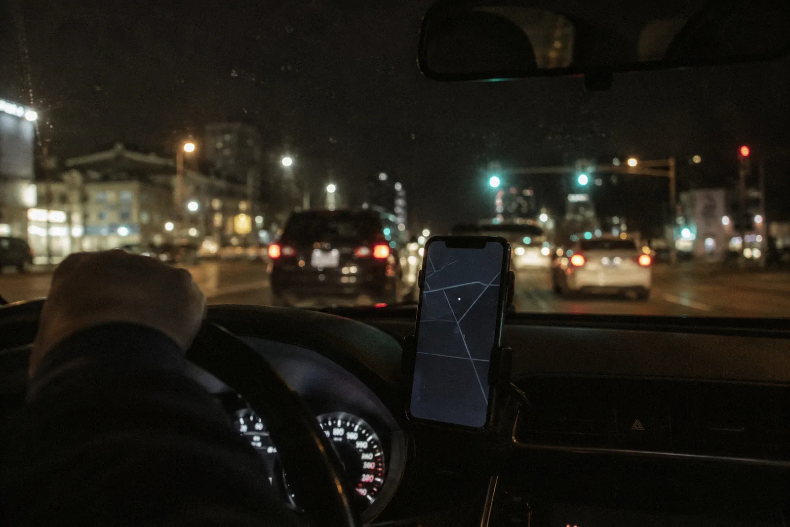 A phone in a dashboard mount showing a blank map screen inside a car at night, city lights through the windshield, no readable text