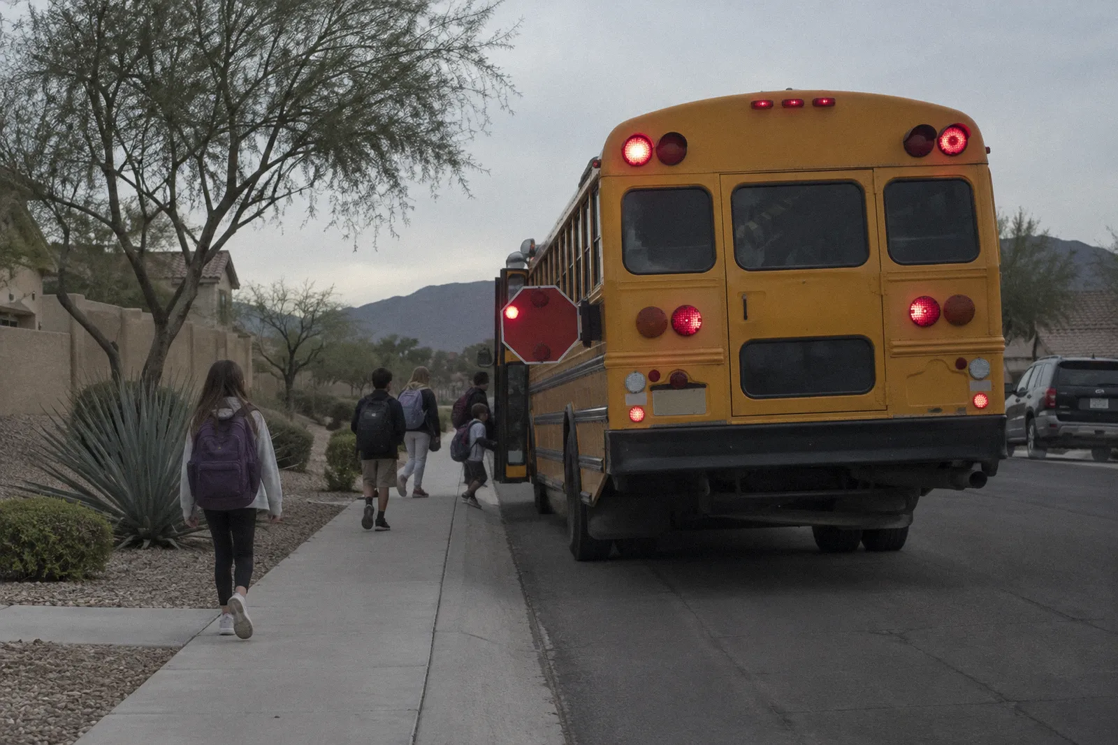 A yellow school bus stopped at a suburban curb with its stop arm out, desert landscaping, no readable lettering