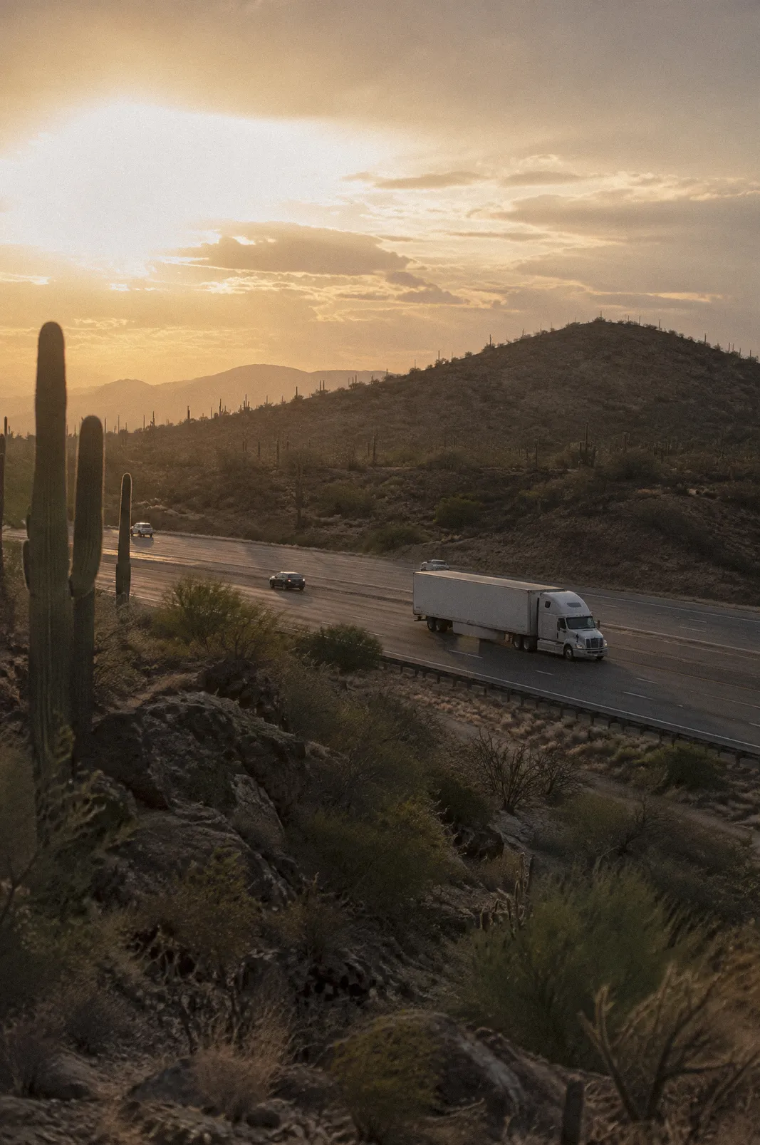 An 18-wheeler crossing a desert interstate at golden hour, long telephoto, saguaros on the hills